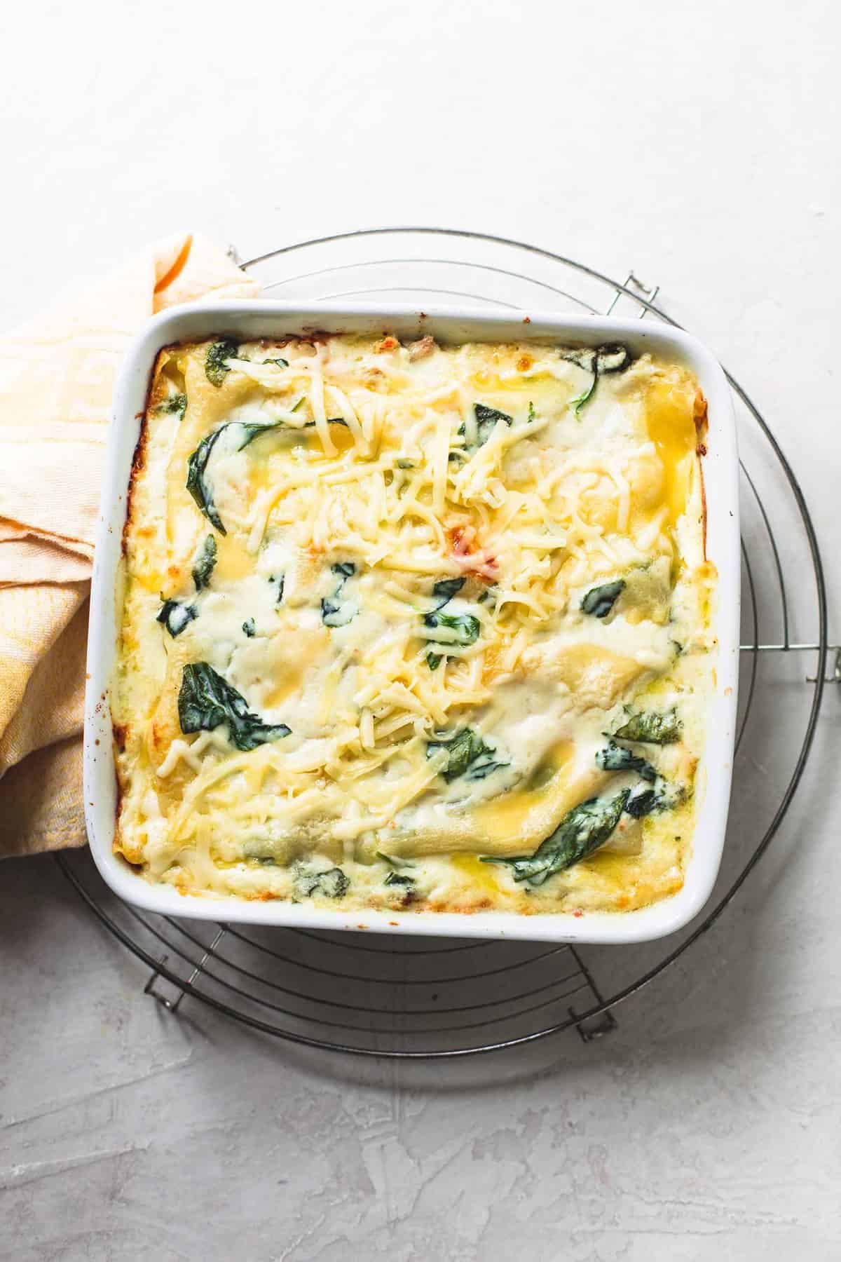 top view of white chicken lasagna with spinach in a baking pan on top of a round cooling rack.