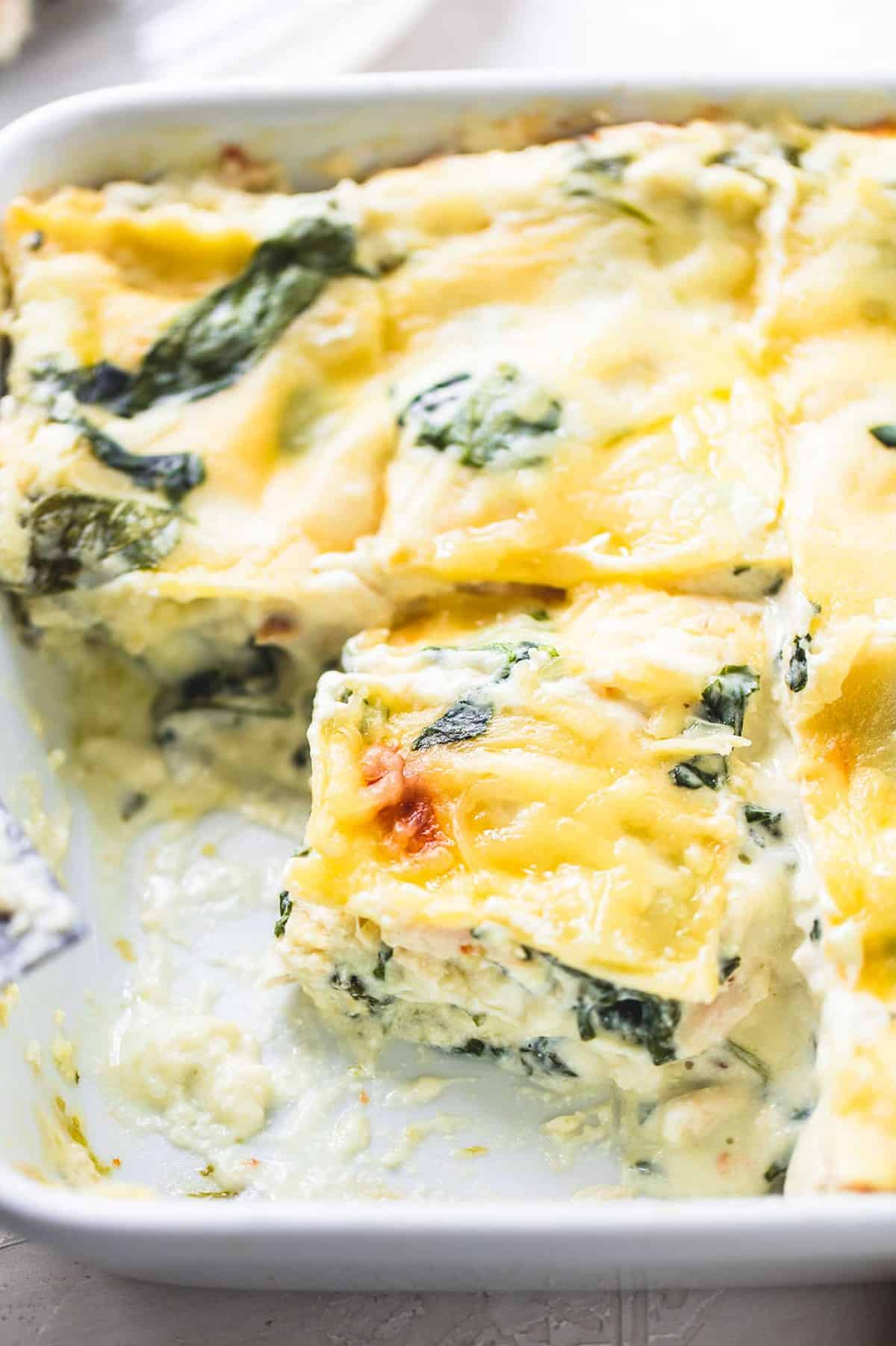 close up top view of white chicken lasagna with spinach with pieces missing in a baking pan.