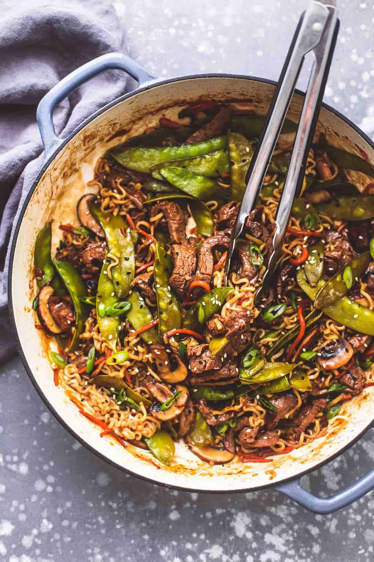 top view of beef noodle stir fry with tongs in a pan.