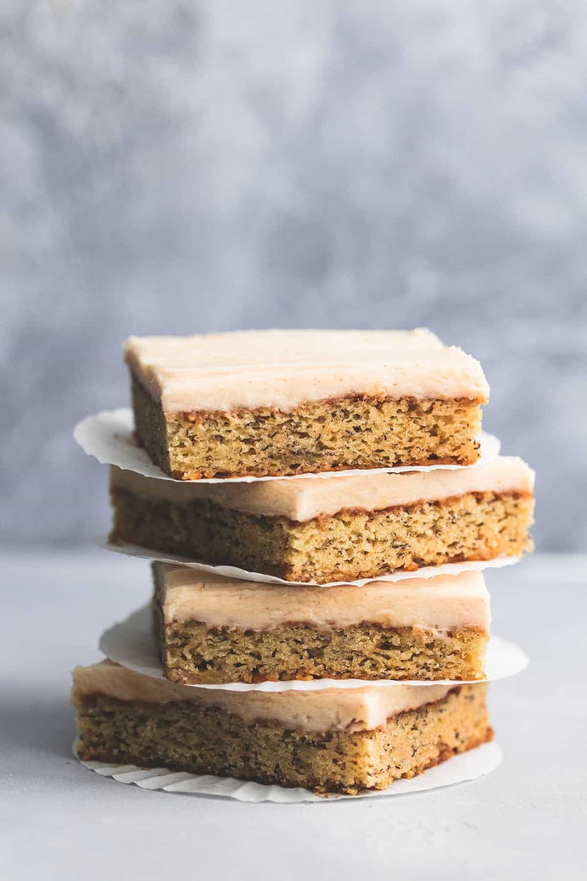 stacked banana bars with cream cheese frosting with a flattened cupcake liner in between each bar.