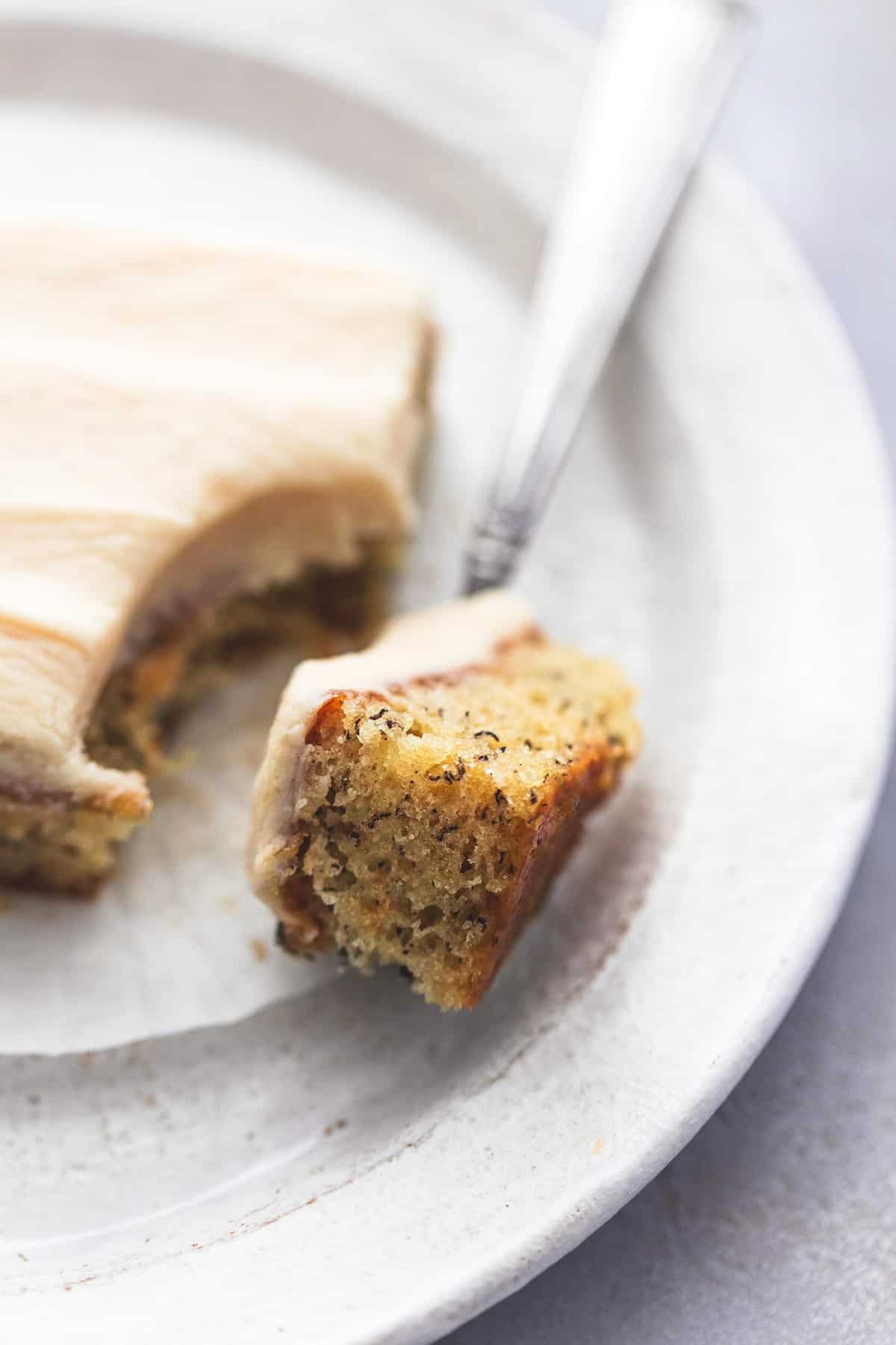 close up of a bite of banana bar with cream cheese frosting on a fork with the rest of the bar on the side all on a plate.