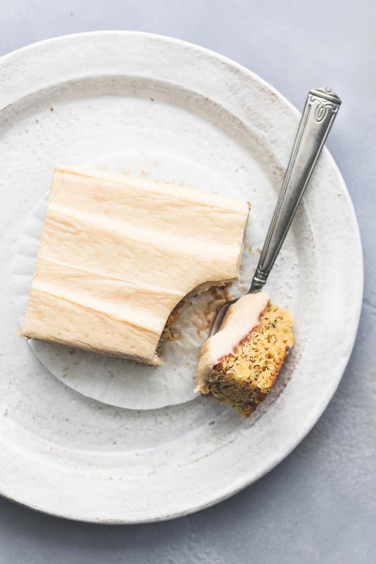 top view of a banana bar with cream cheese frosting with a bite on a fork on the side all on a plate.