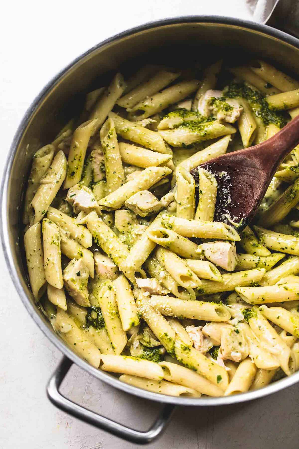 top view of creamy pesto chicken pasta with a wooden serving spoon in a pot.