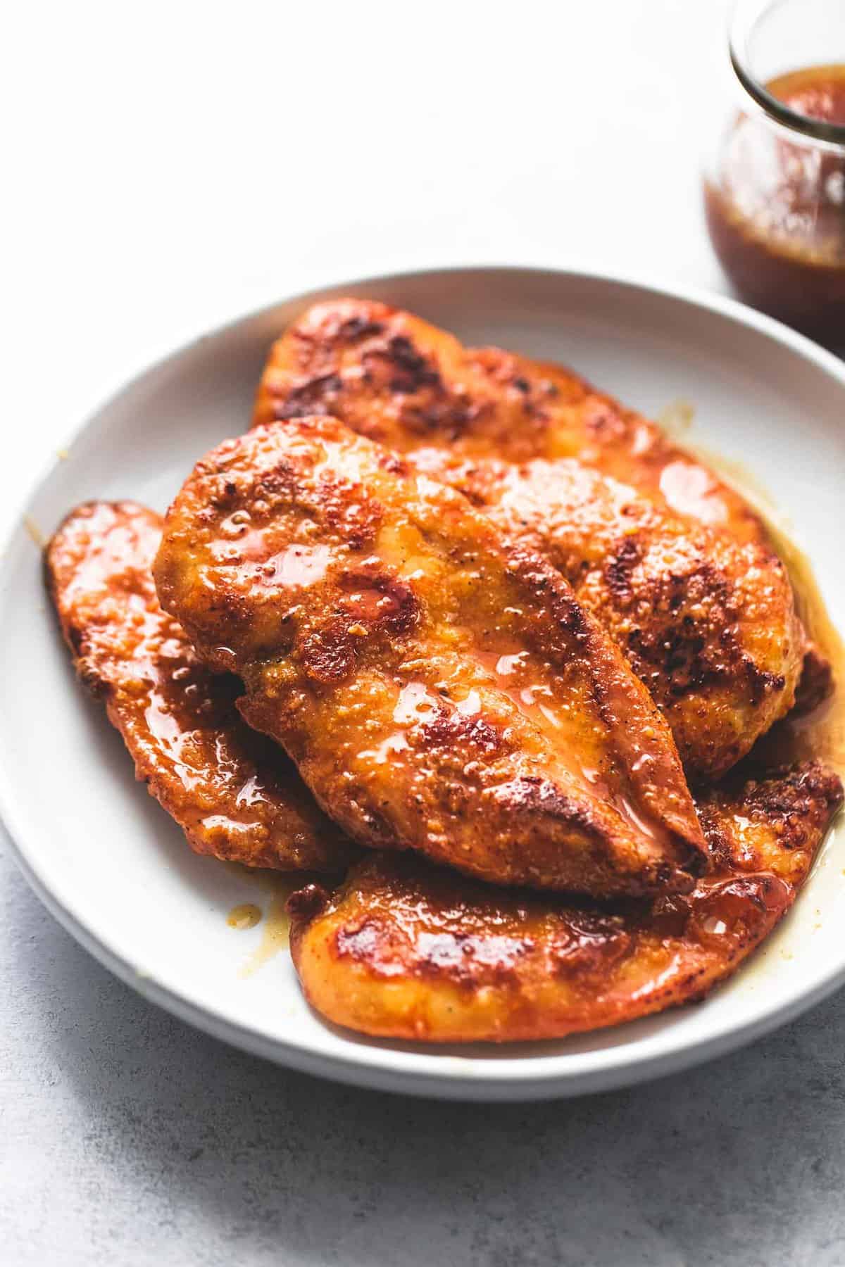 crispy honey garlic chicken on a plate with sauce in a glass jar on the side.