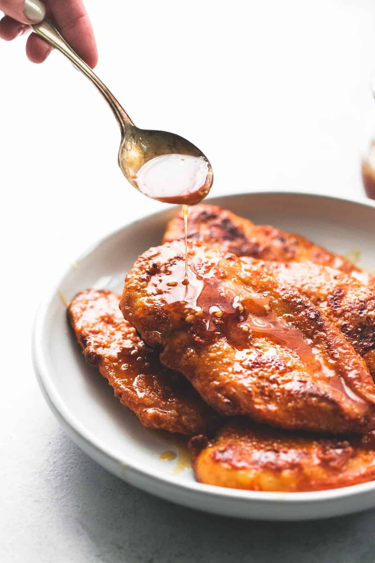 a spoon pouring sauce on top of crispy honey garlic chicken on a plate.