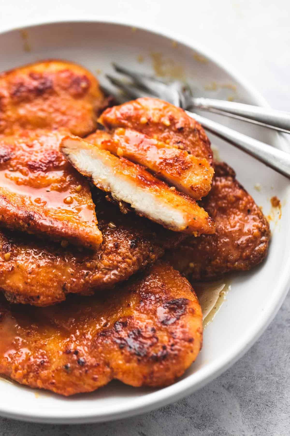 close up of crispy honey garlic chicken with some chicken cut up and two forks on the side all on a plate.