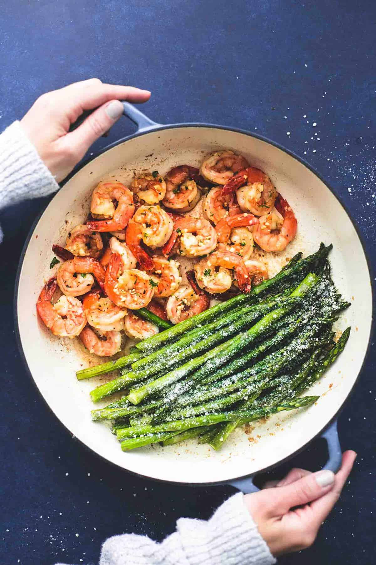 top view of hands holding a pan of one pan shrimp and asparagus.