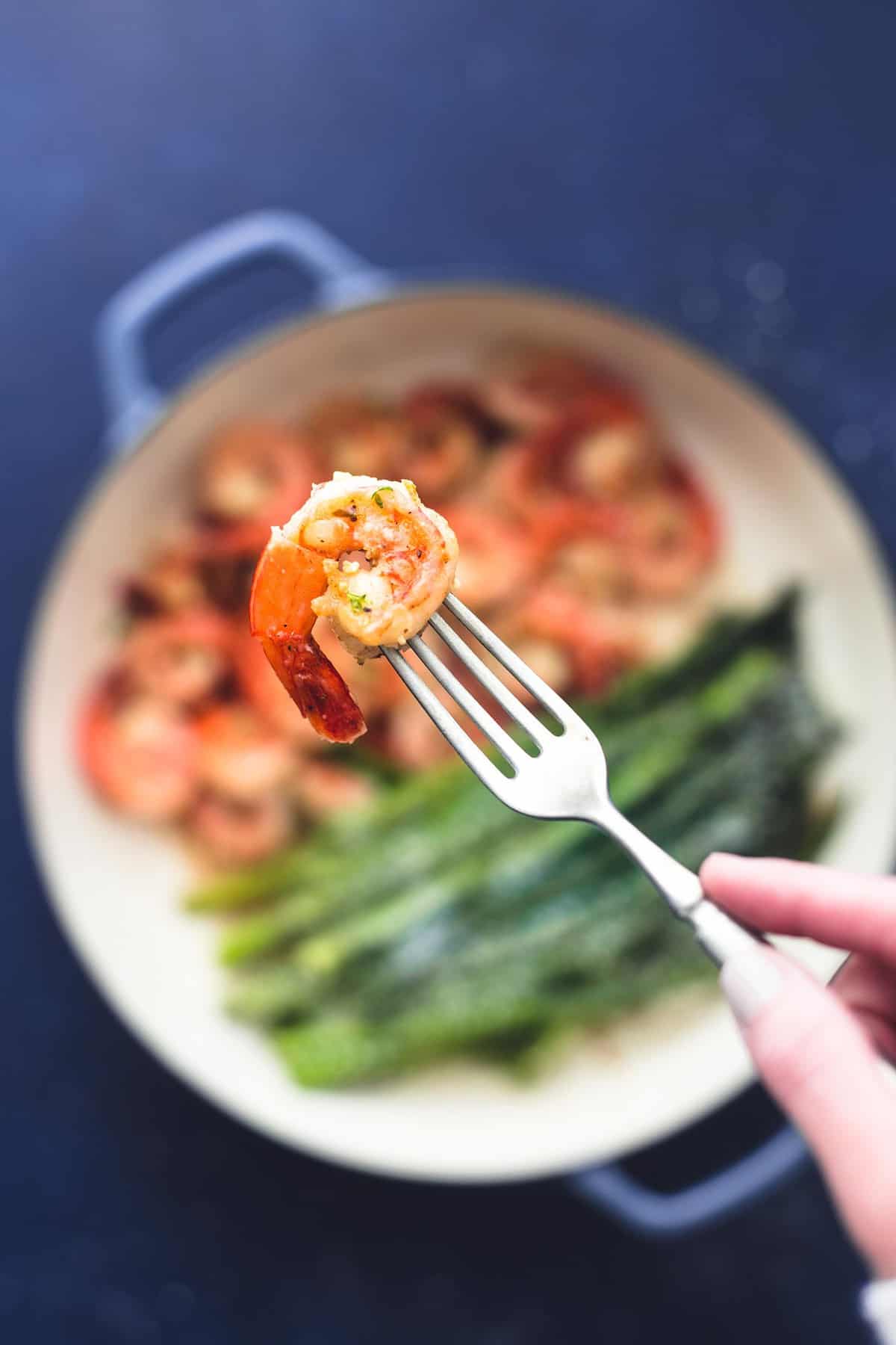 a piece of shrimp on a fork being held above a pan of one pan shrimp and asparagus.