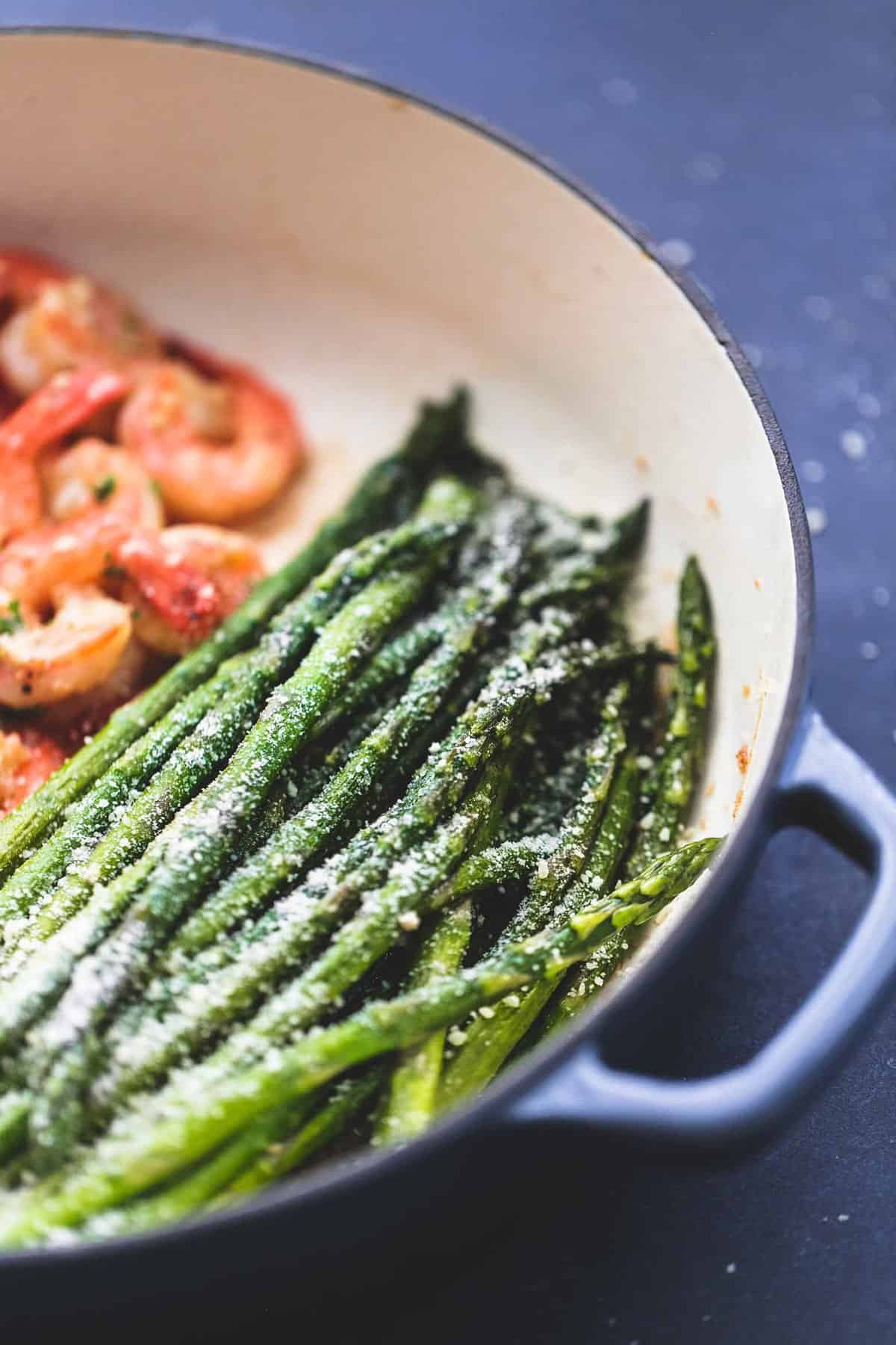 close up of asparagus with shrimp on the side in a pan.