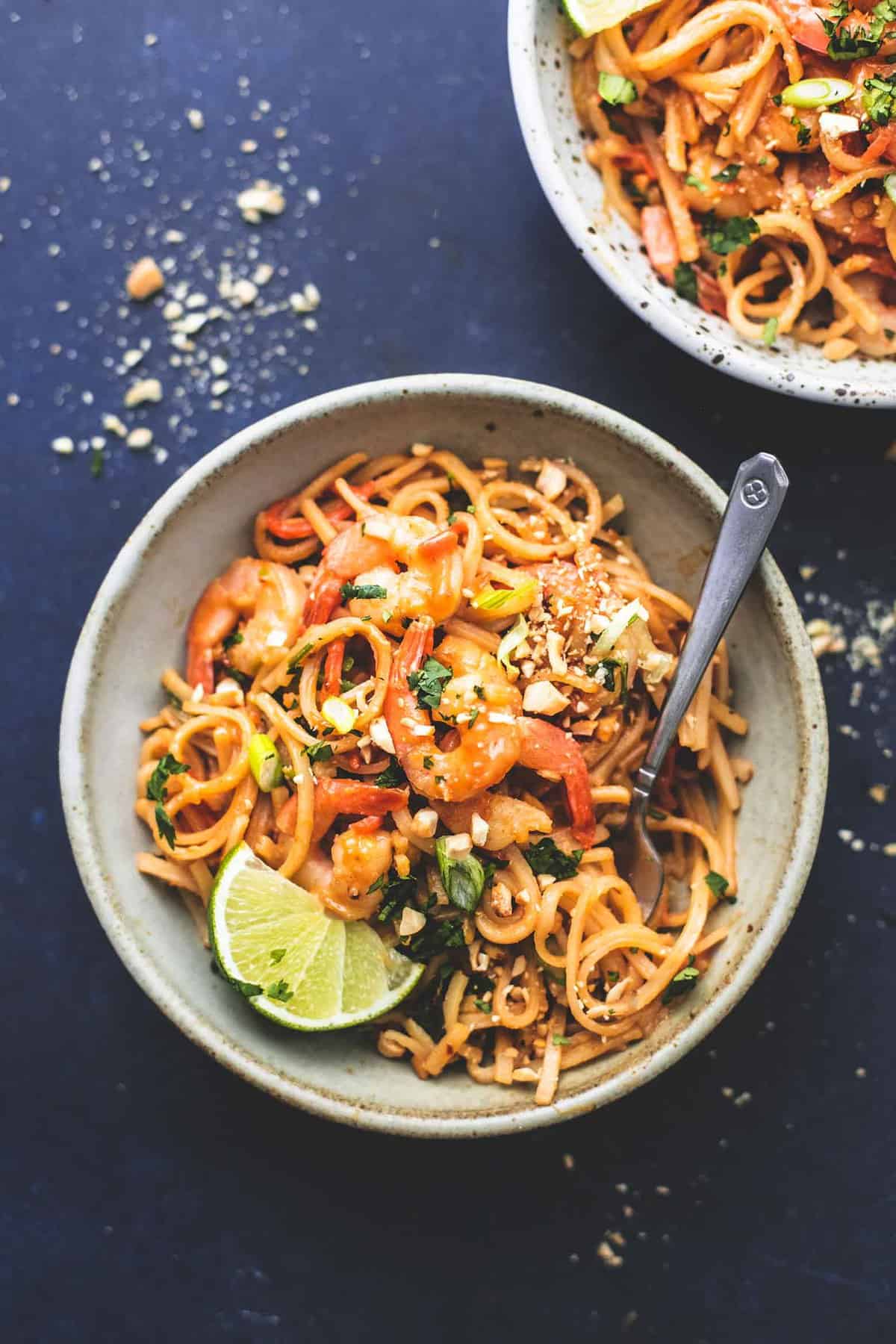 top view of shrimp pad Thai with peanut sauce with a fork in a bowl with another bowl on the side.