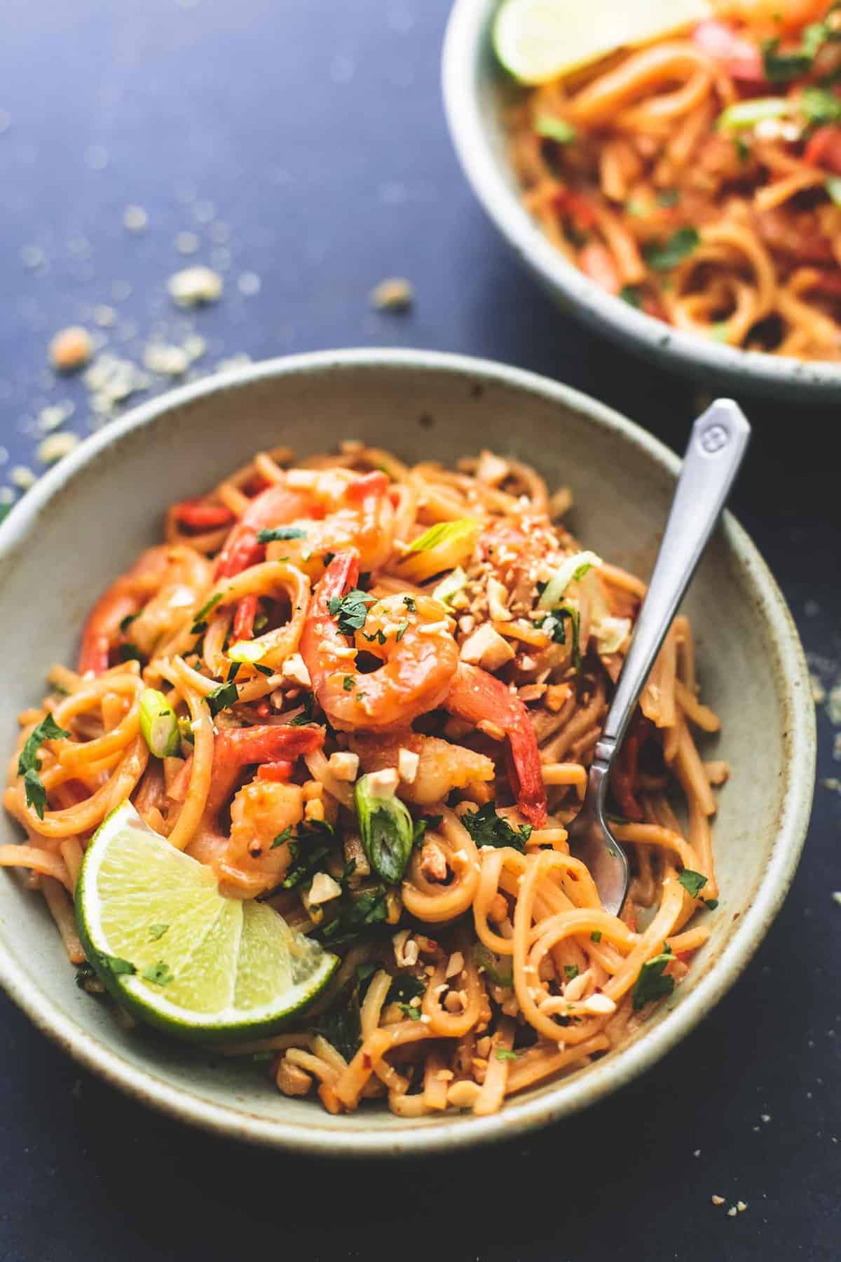 shrimp pad Thai with peanut sauce with a fork in a bowl with a mother bowl faded in the background.