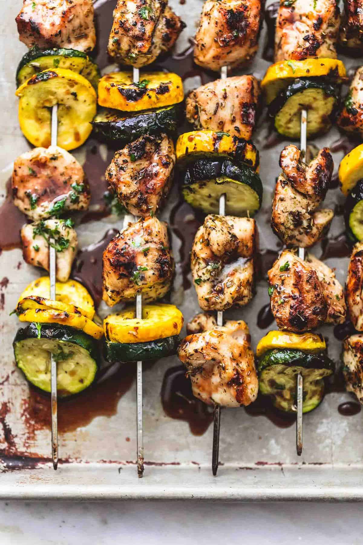 close up top view of balsamic chicken and veggie kabobs in a baking sheet.
