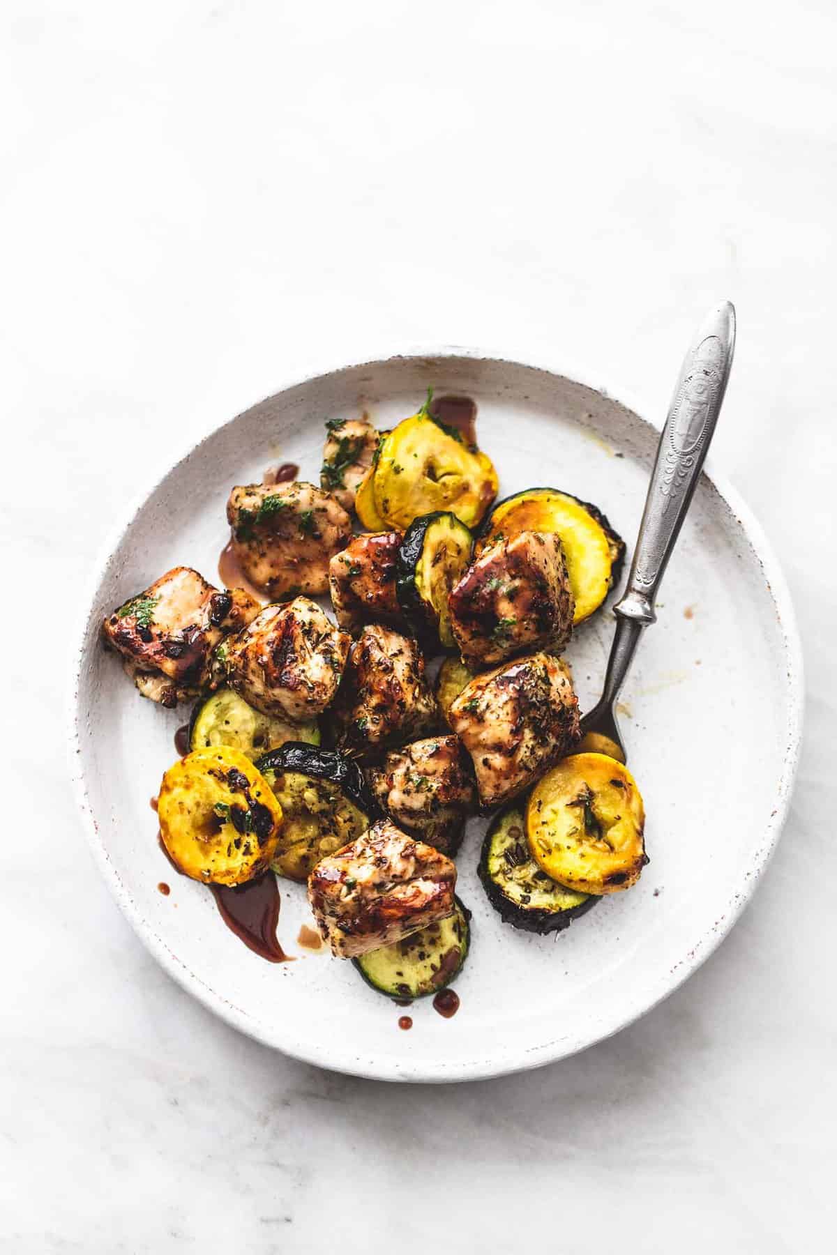 top view of deconstructed balsamic chicken and veggie kabobs with a bite on a fork on a plate.