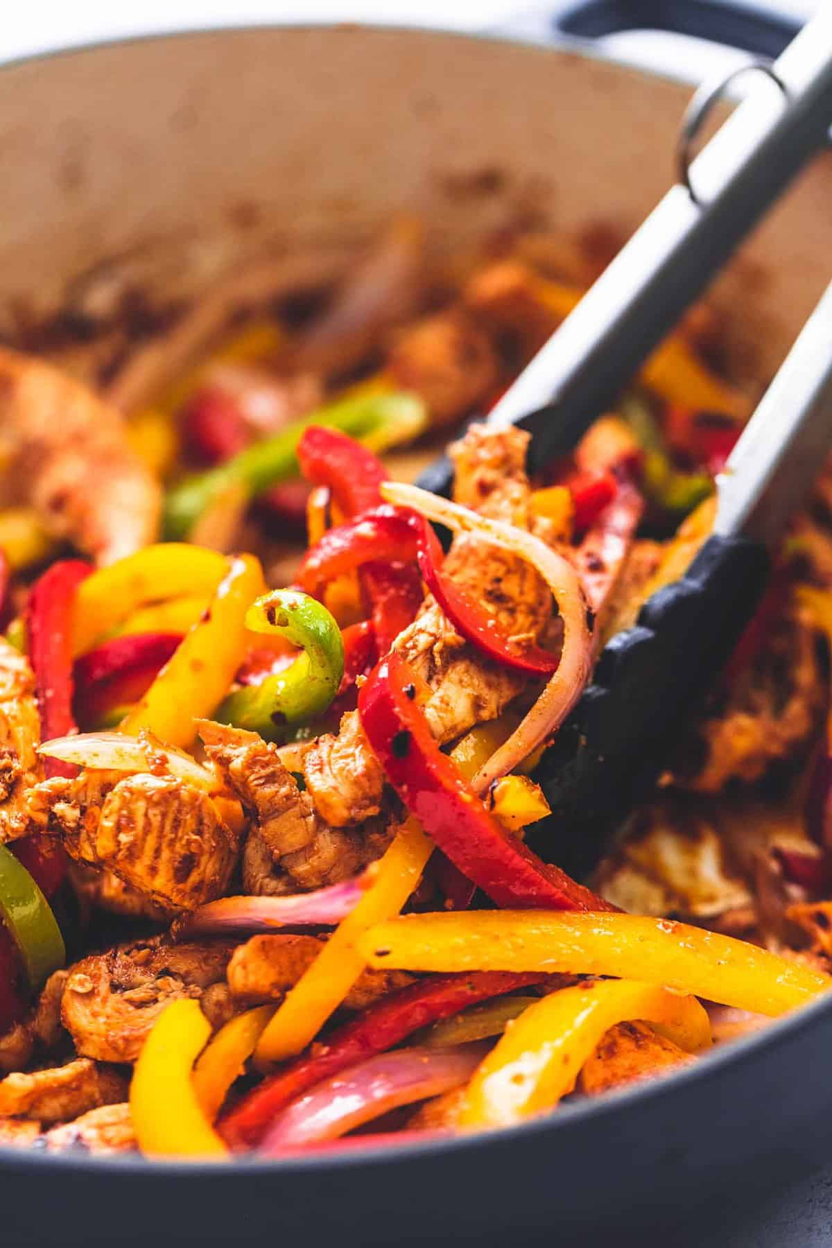 close up of tongs grabbing chicken fajitas skillet.