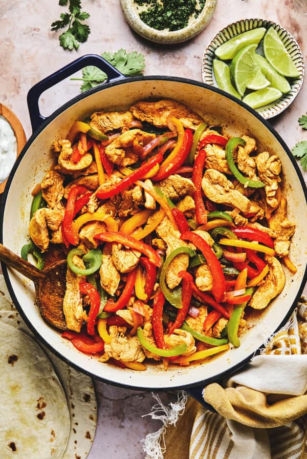 Chicken fajita filling in skillet on table surrounded by toppings in pinch bowls.