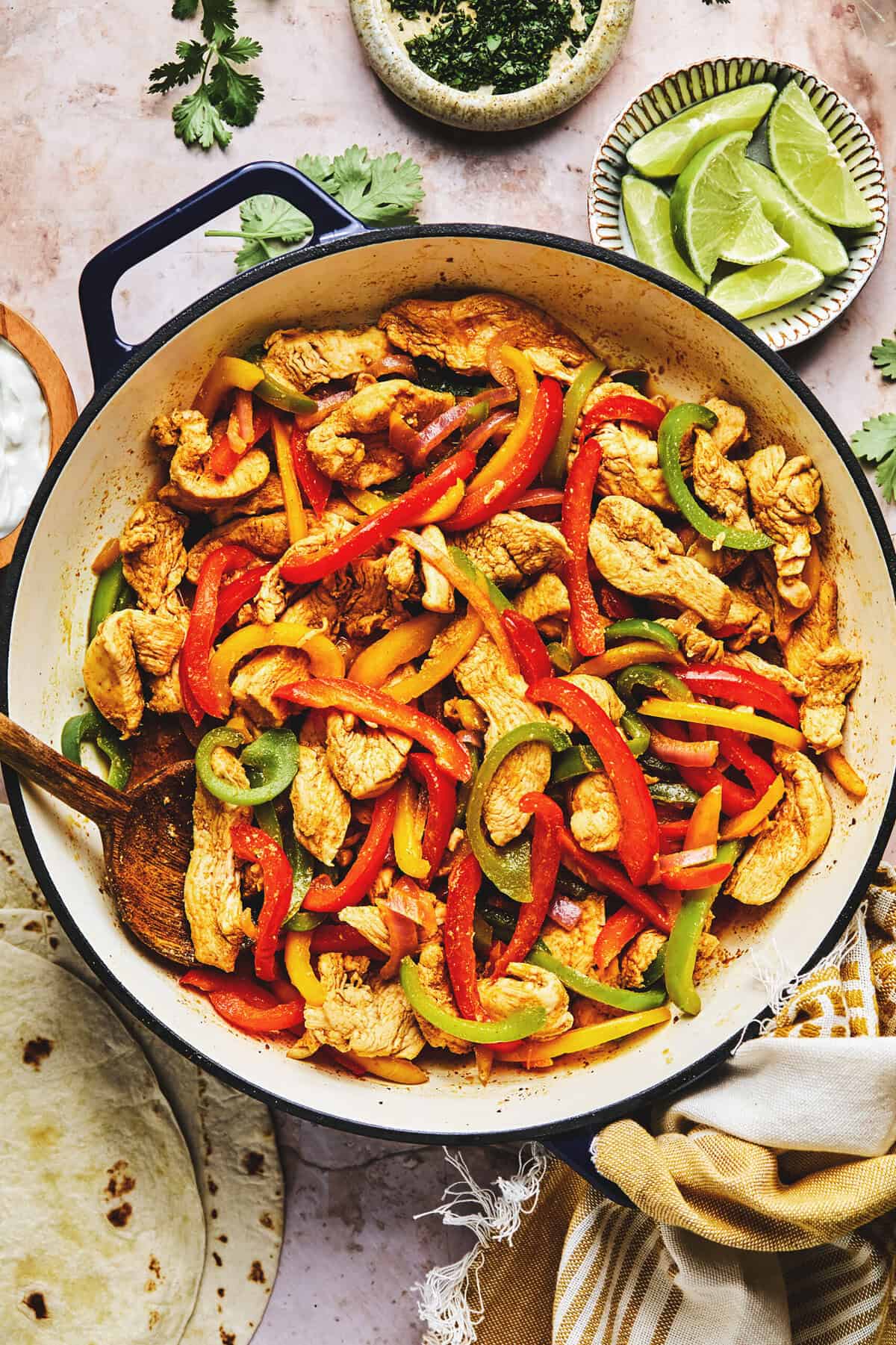 Chicken fajita filling in skillet on table surrounded by toppings in pinch bowls.