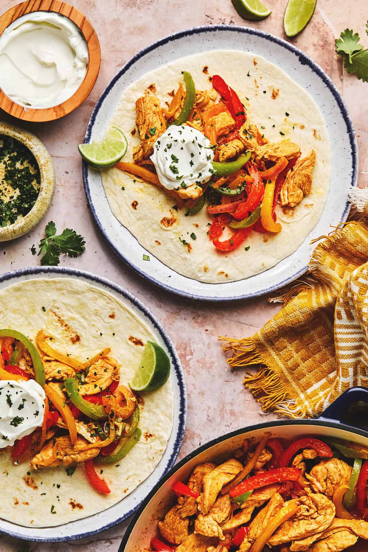 Tortillas on plates filled with cooked bell peppers, chicken, and onions, topped with sour cream.