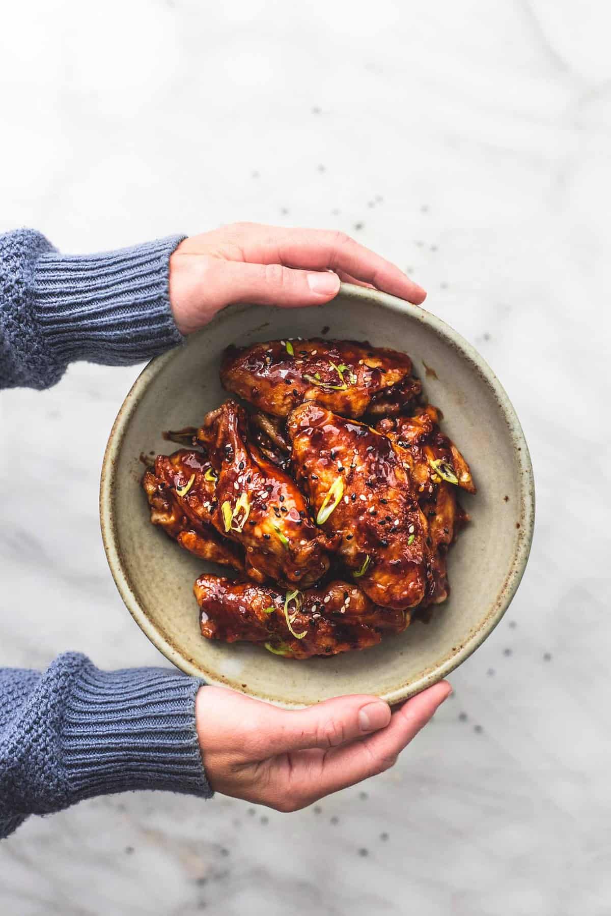 hands holding a plate of spicy Korean bbq chicken wings.