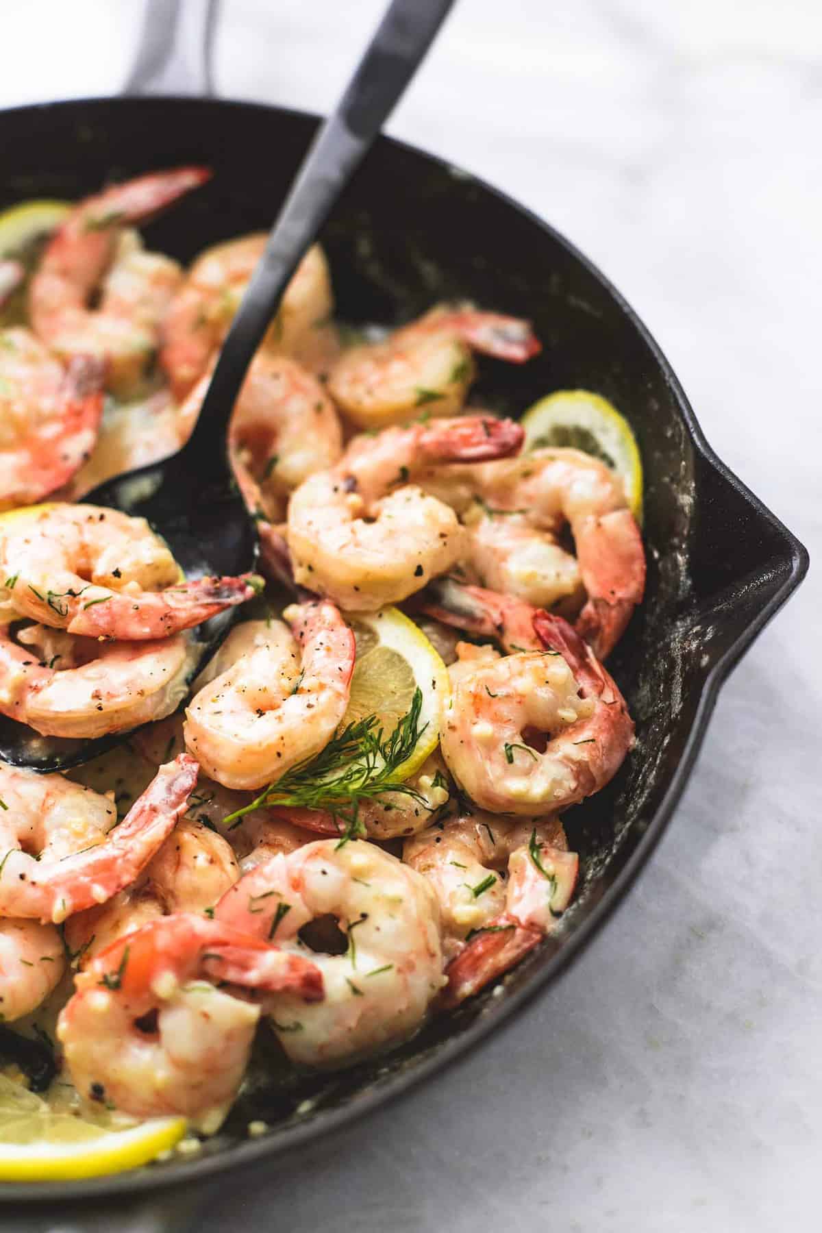 close up of creamy lemon dill shrimp with a serving spoon in a pan.
