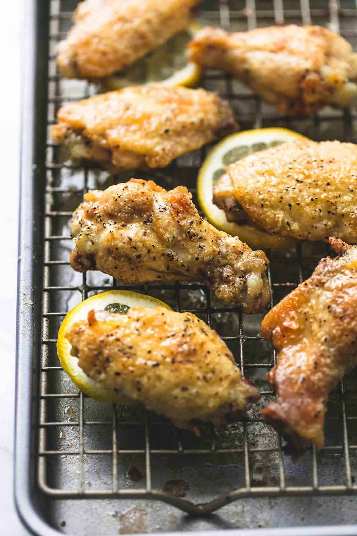 close up of baked lemon pepper chicken wings and lemon wheels on a cooling rack on a baking sheet.