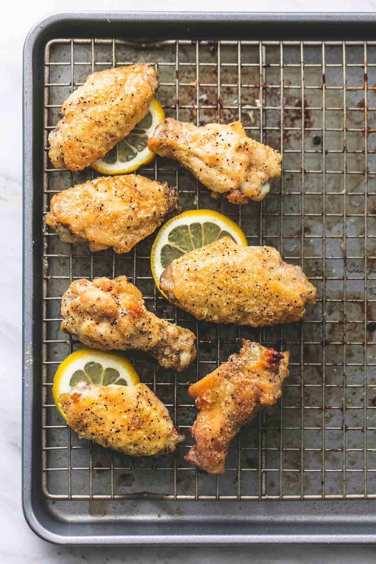 top view of baked lemon pepper chicken wings with lemon wheels underneath some of the wings all on a cooling rack on a baking sheet.