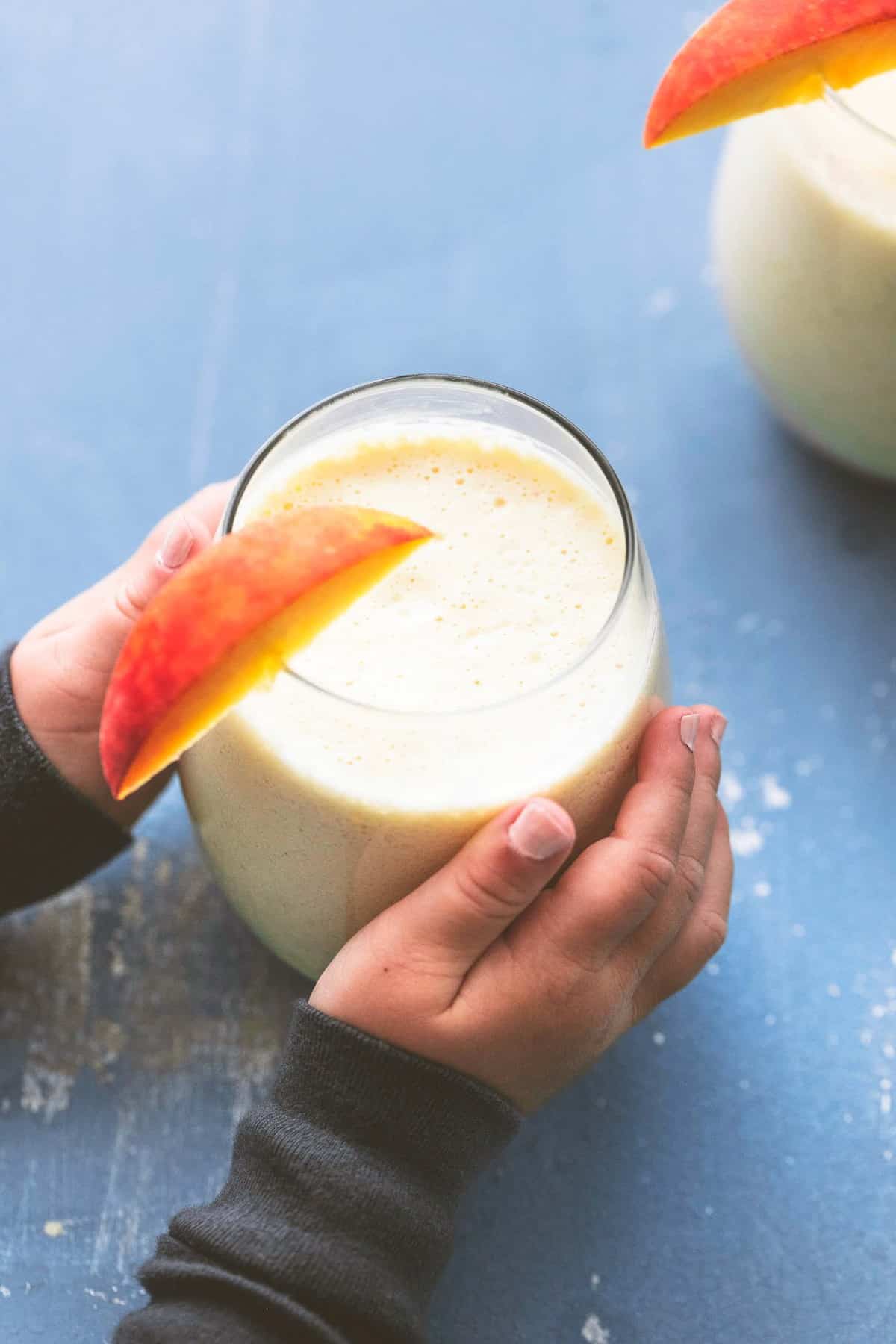 a child's hands grabbing a glass of peaches n cream moon milk with a peach slice on top.