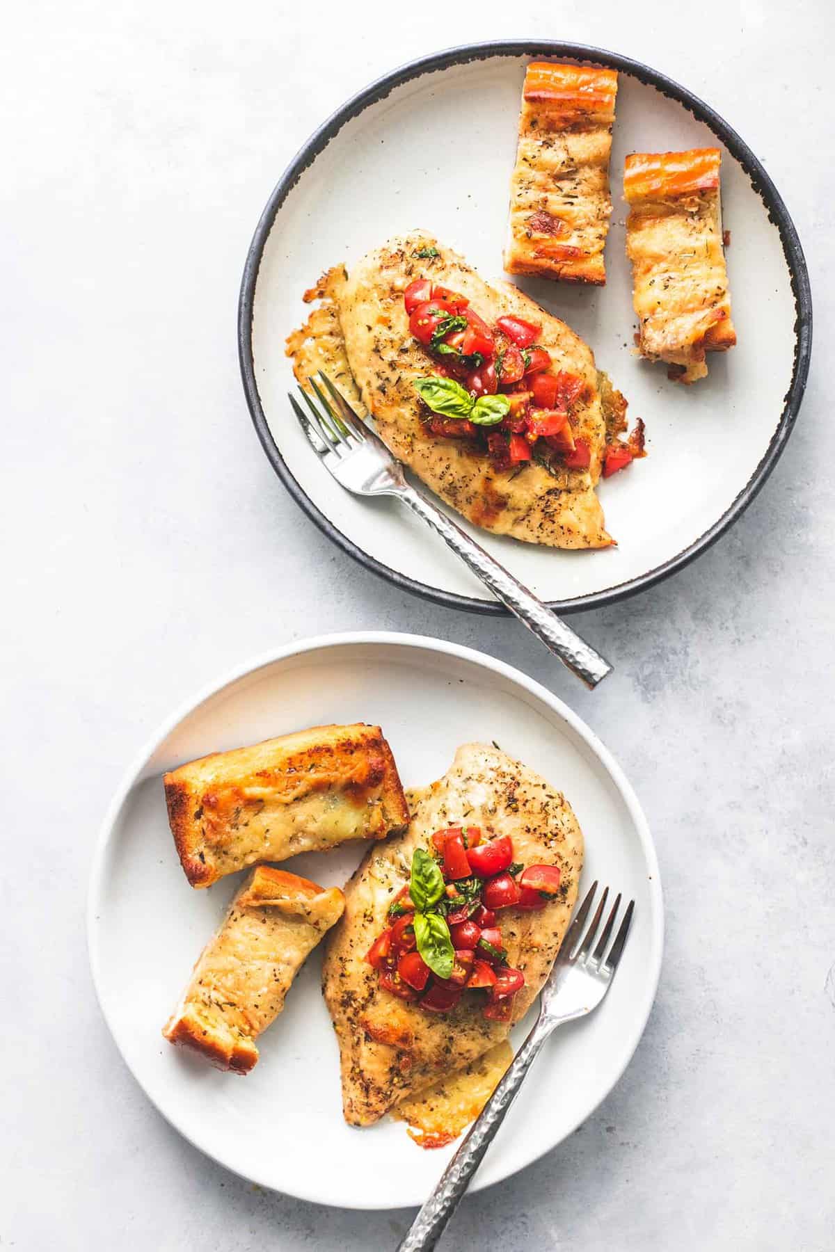 top view of two plates with sheet pan bruschetta chicken and cheesy garlic bread and forks on them.