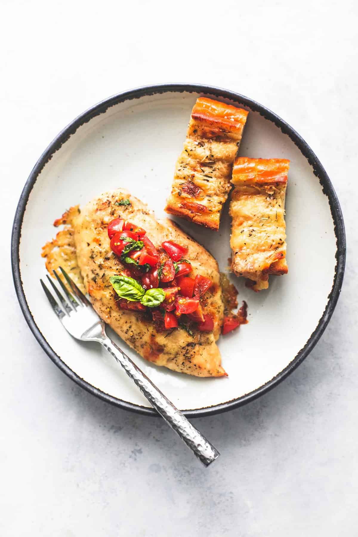 top view of sheet pan bruschetta chicken and cheesy garlic bread with a fork on a plate.