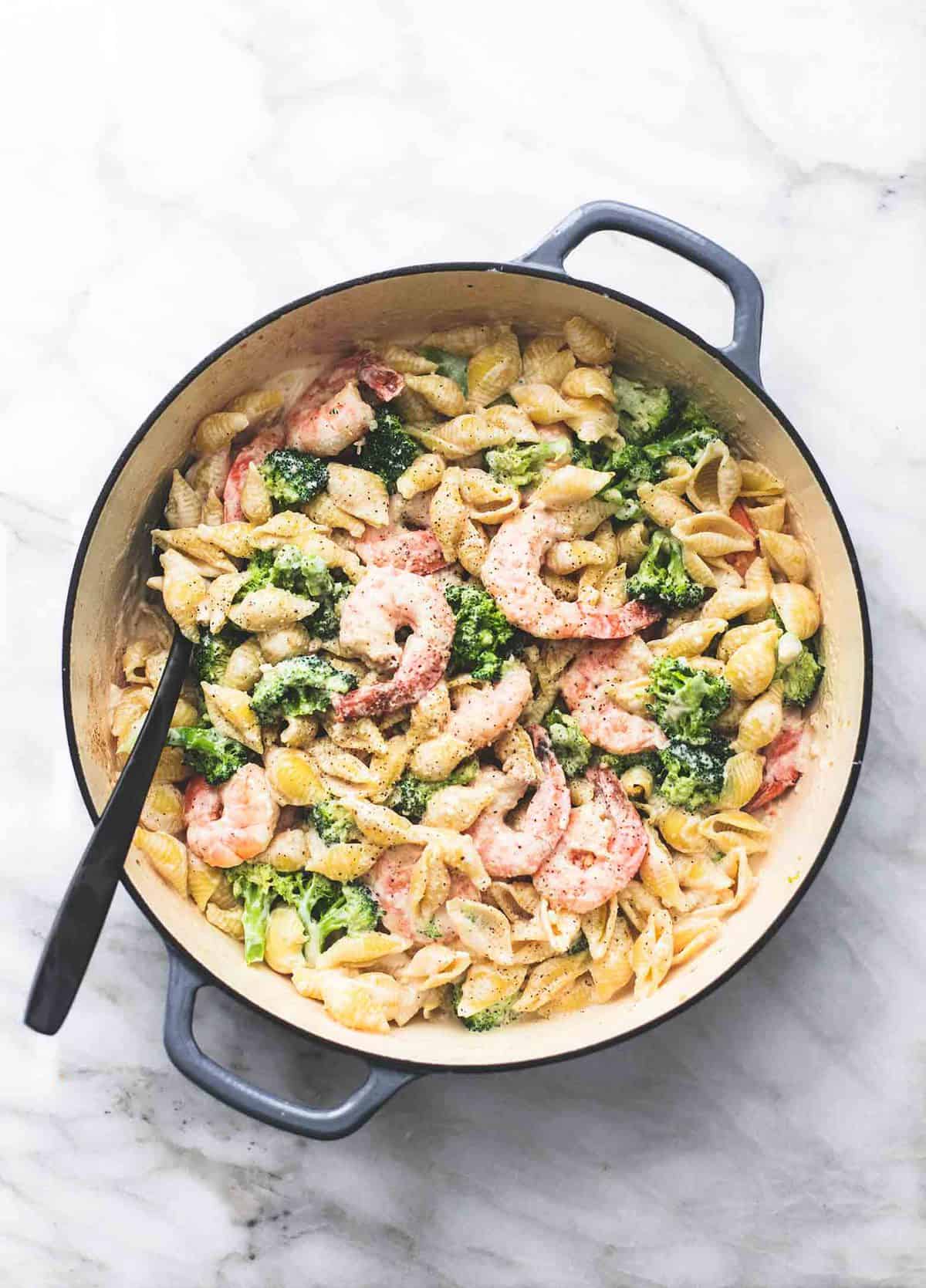 top view of shrimp and broccoli alfredo with a serving spoon in a pan.