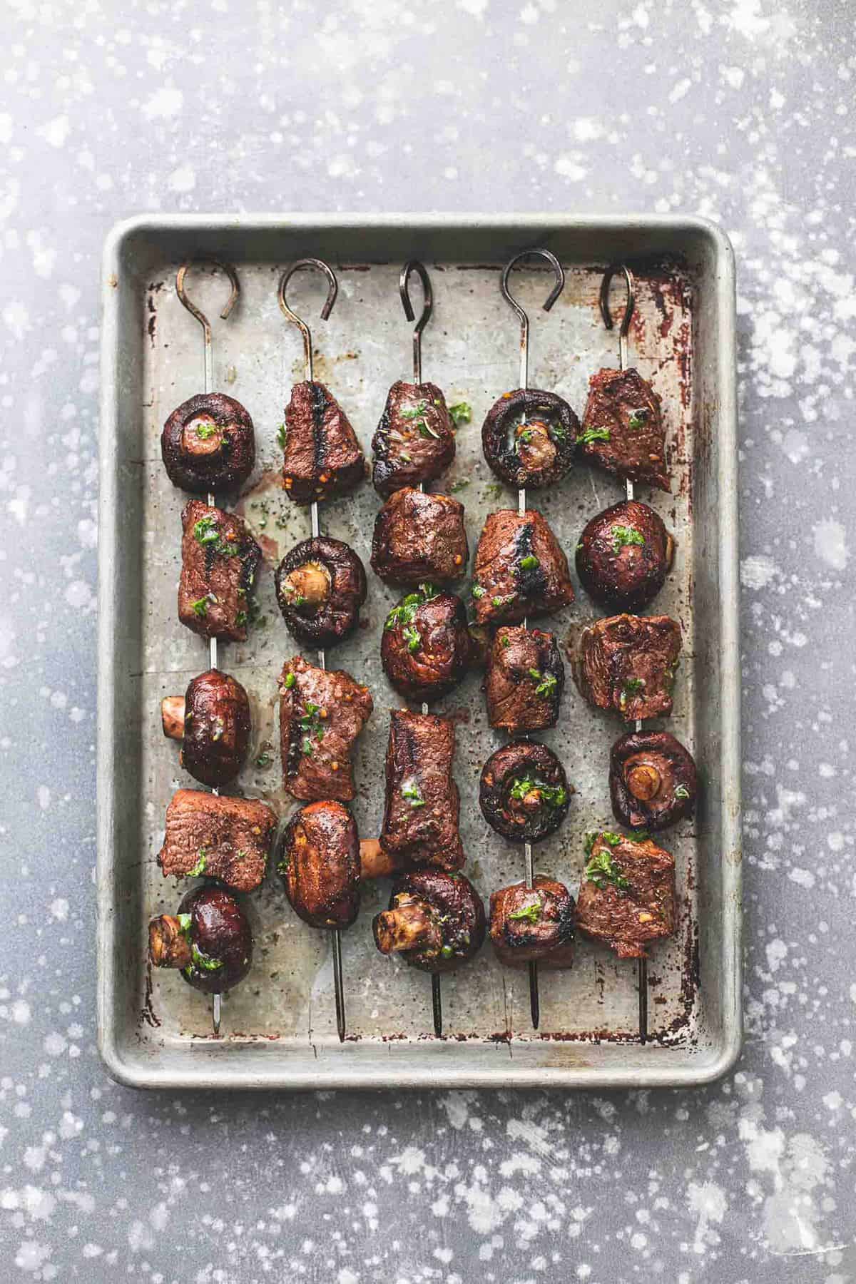 top view of grilled steak and mushroom kabobs on a baking sheet.