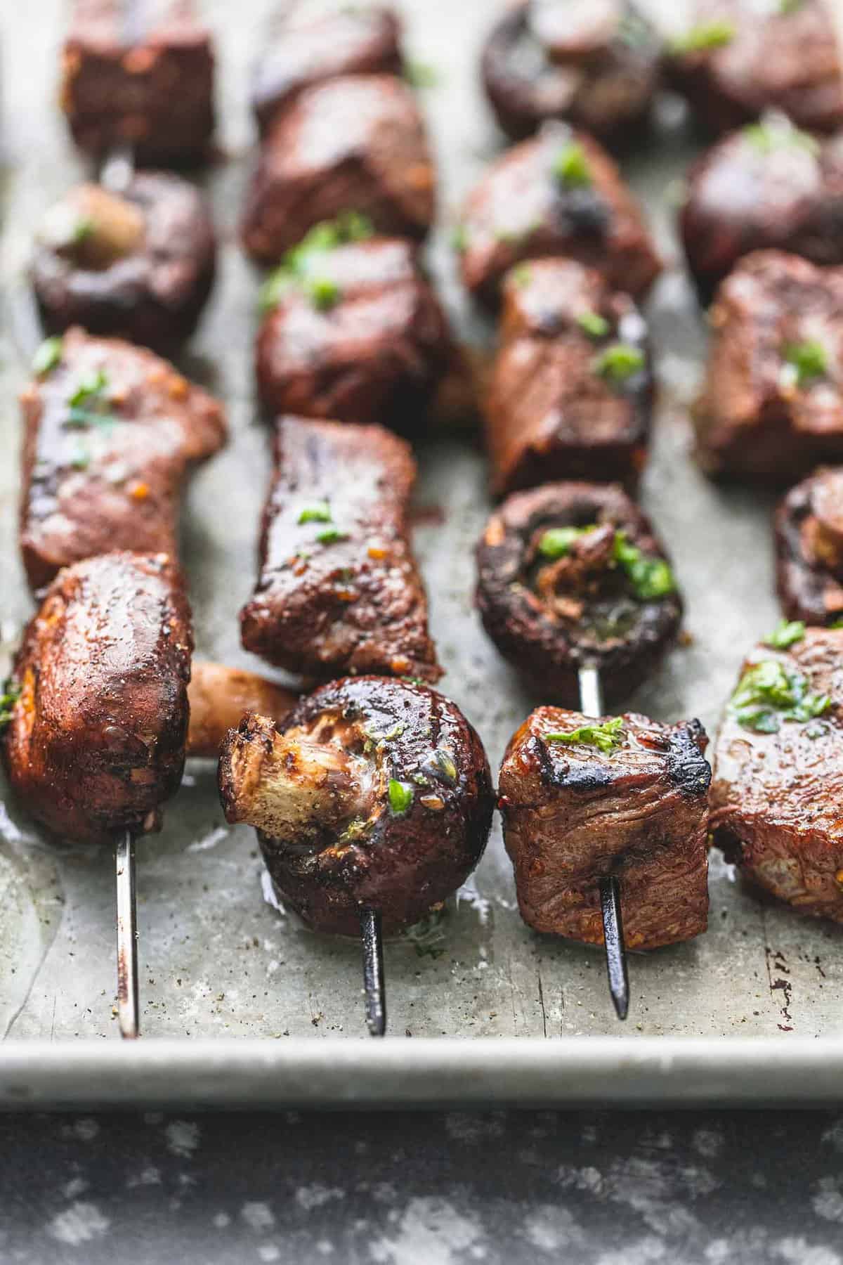 close up of grilled steak and mushroom kabobs on a baking sheet.