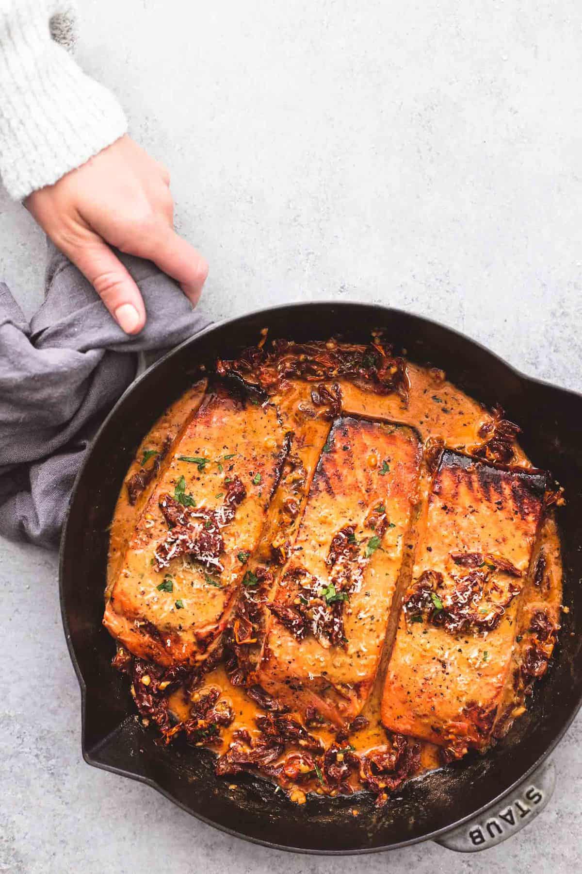 top view of salmon in creamy sun dried tomato sauce in a pan with a hand holding the handle.