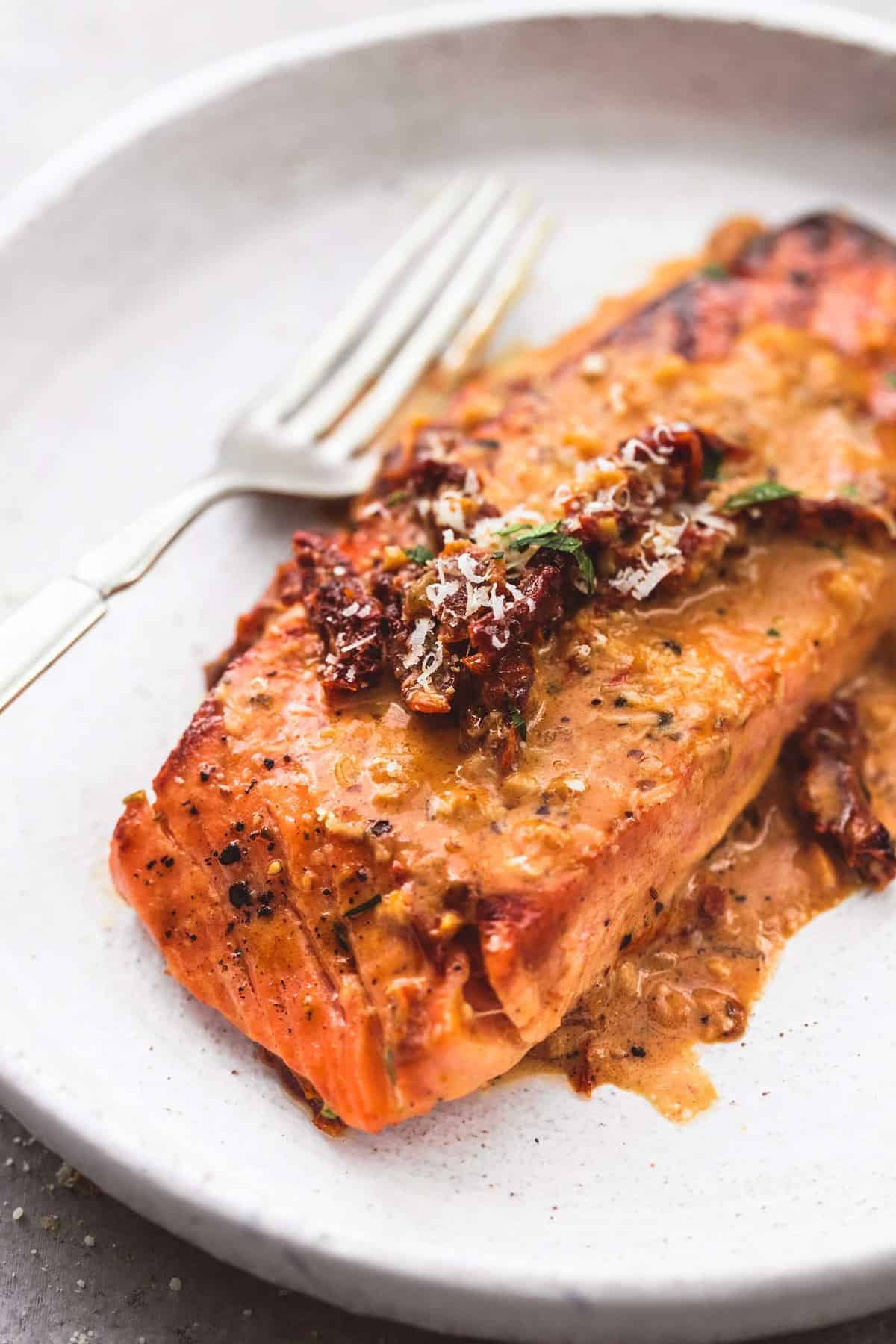 close up of salmon in creamy sun dried tomato sauce with a fork on a plate.