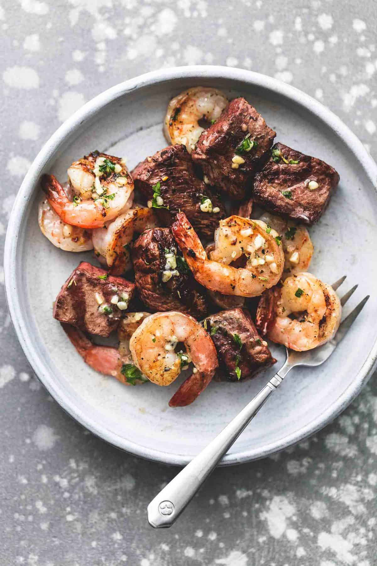 top view of deconstructed garlic butter surf and turf kabobs with a fork on a plate.