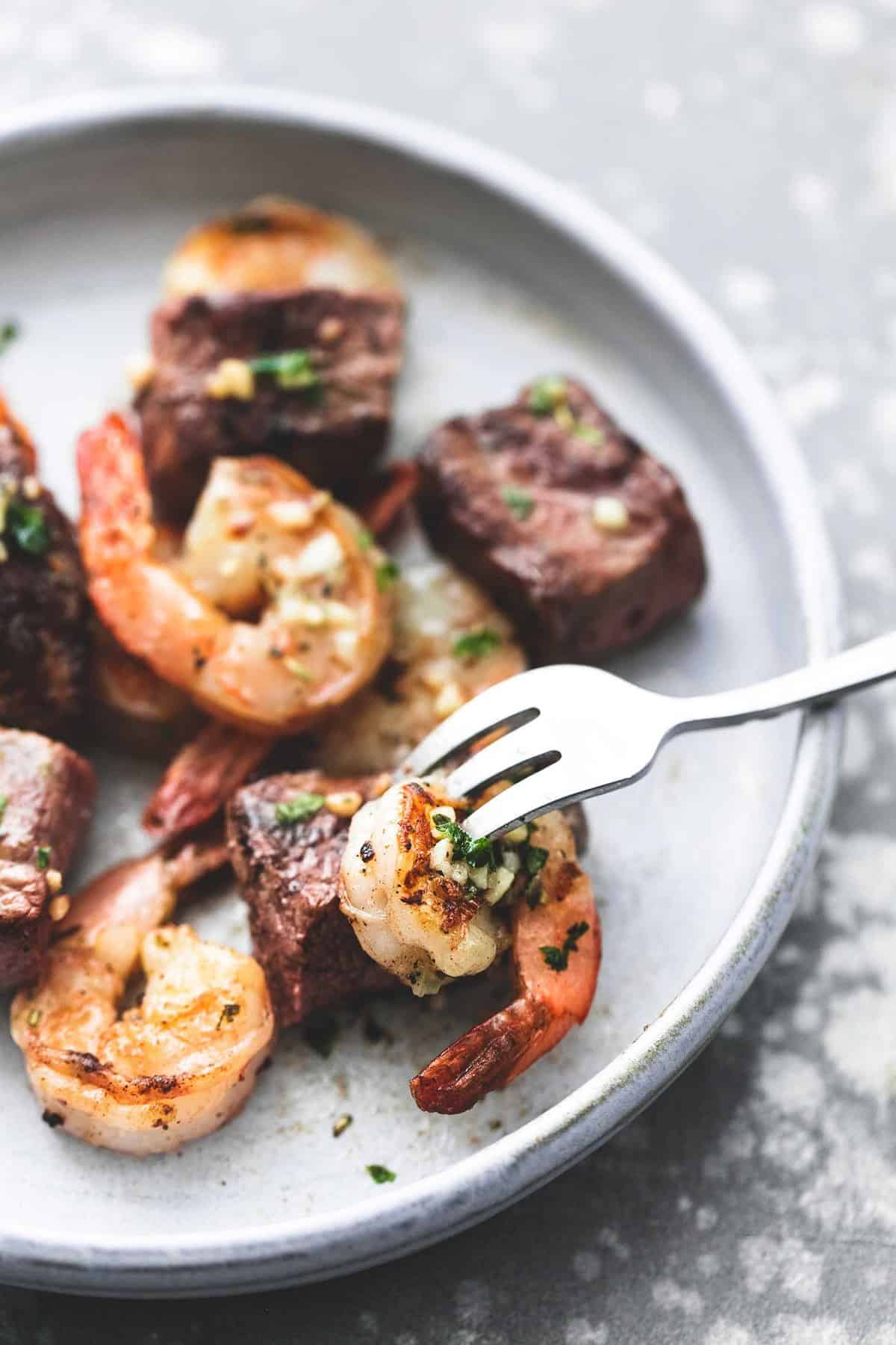 close up of a fork grabbing a bite of deconstructed garlic butter surf and turf kabobs on a plate.