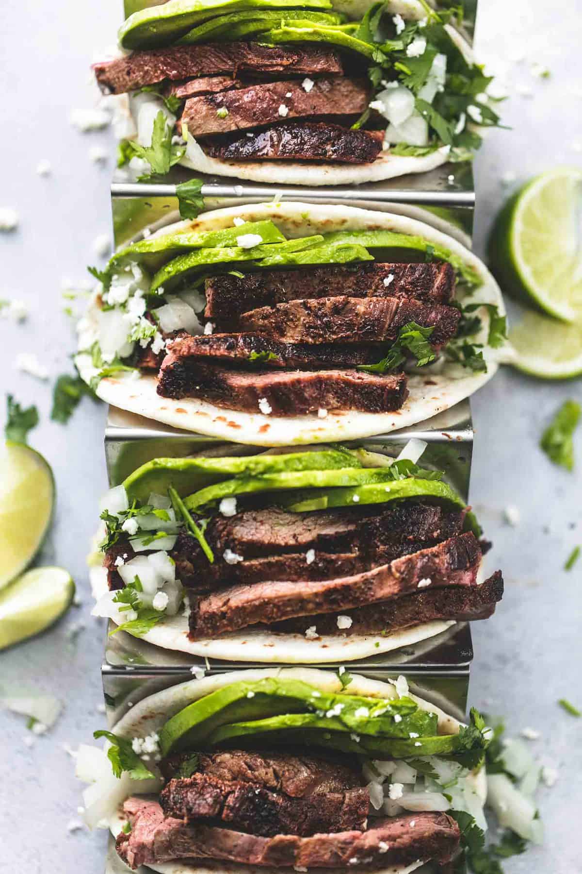 top view of flank steak tacos on a taco rack with lime slices on the side.