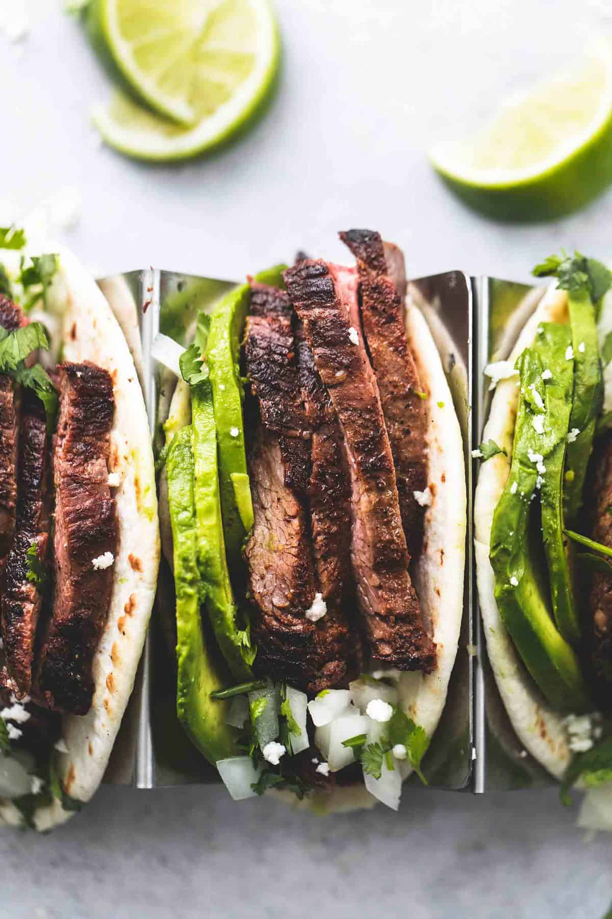 close up top view of flank steak tacos on a taco rack with lime slices on the side.