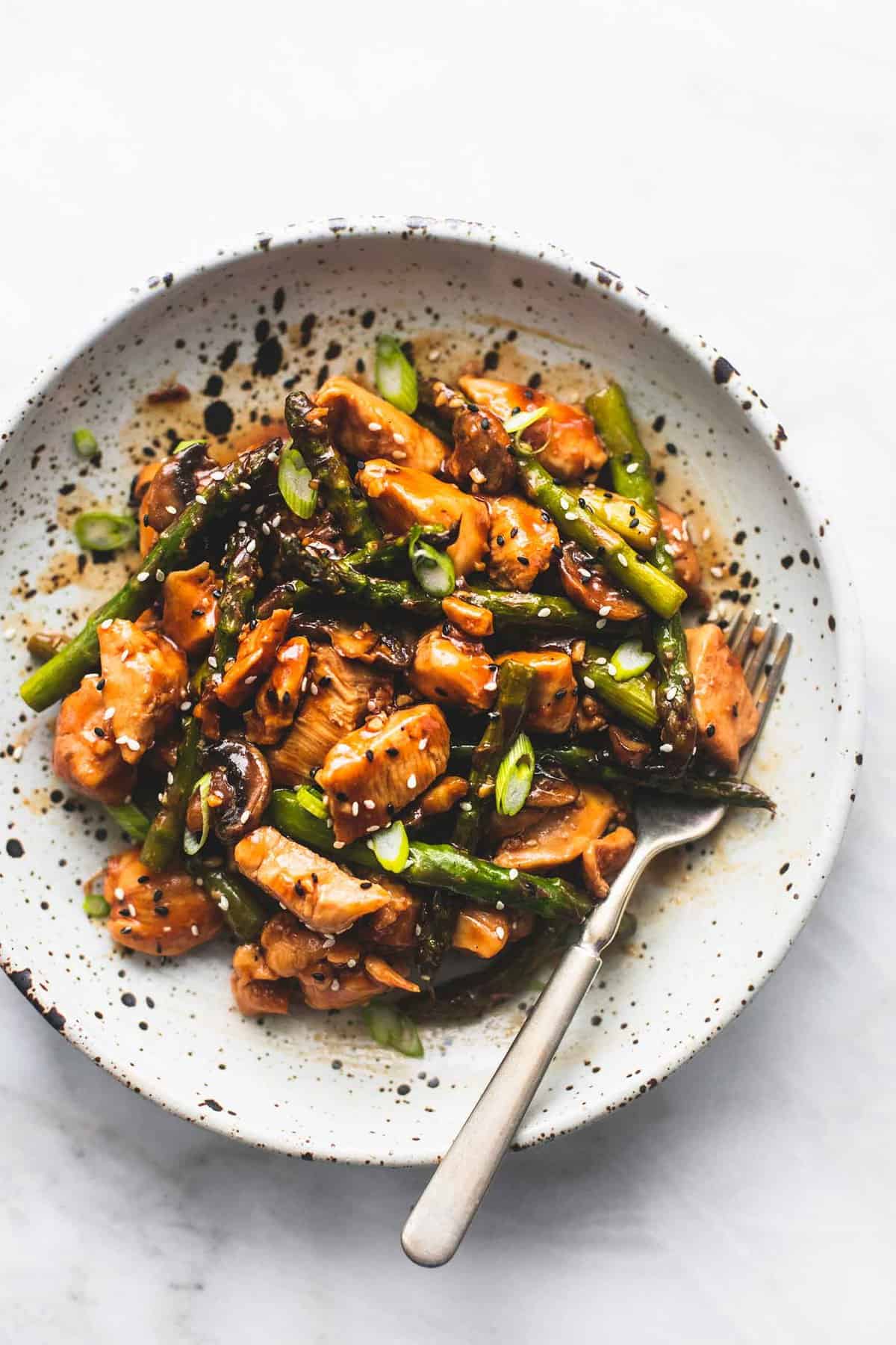 top view of chicken and asparagus stir fry with a fork on a plate.