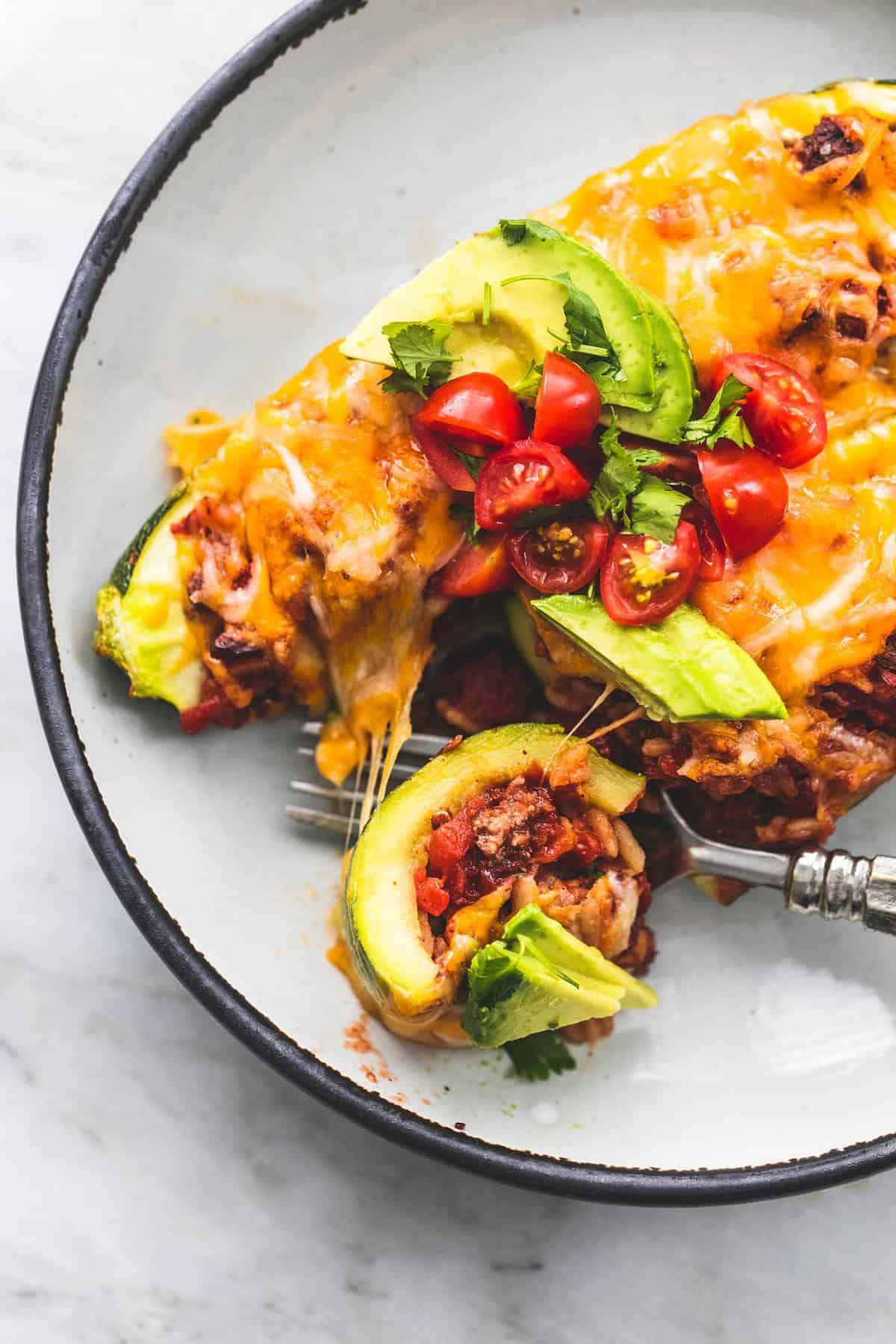 close up of taco stuffed zucchini boats with a fork separating a bite from one of the boats all on a plate.