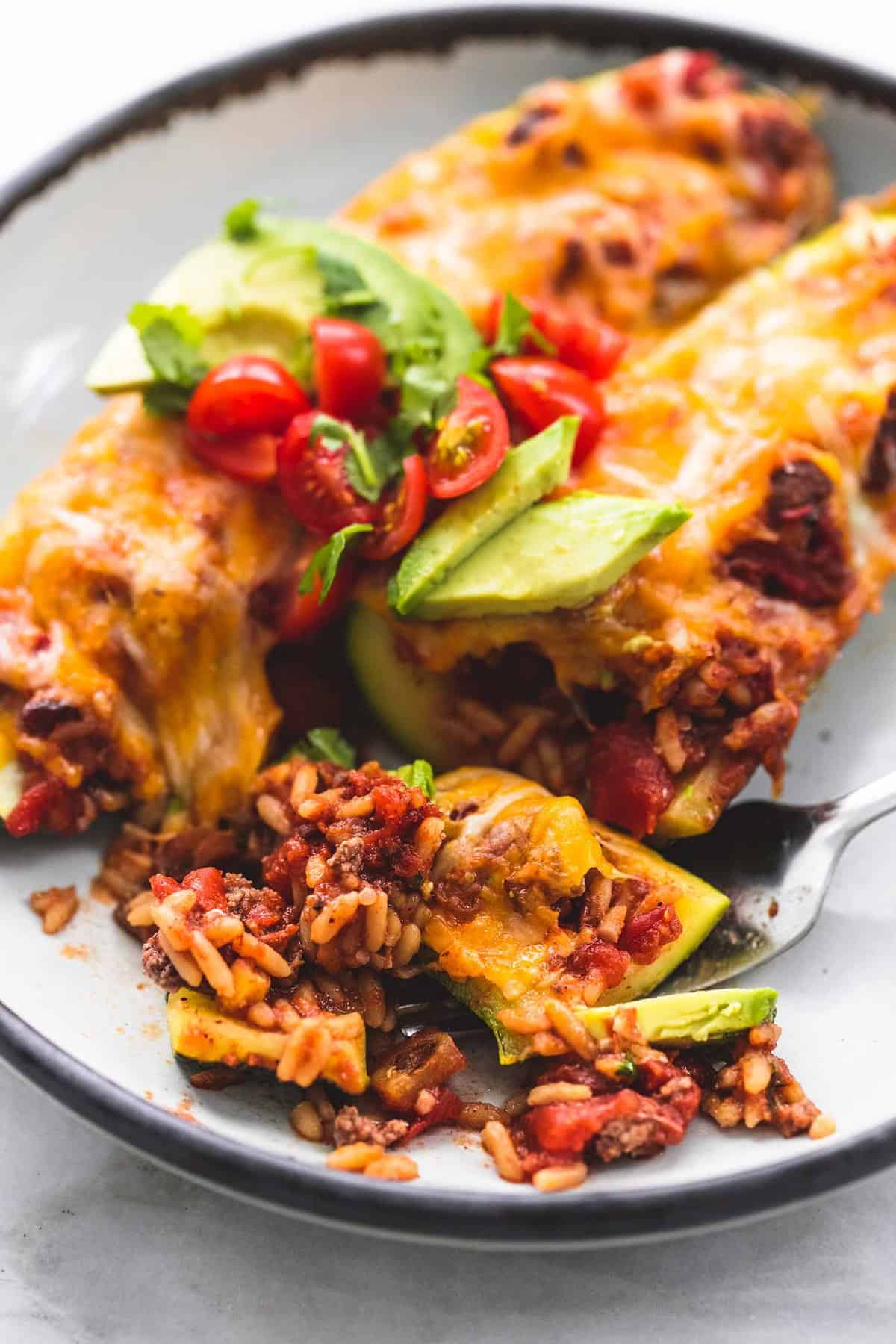 close up of taco stuffed zucchini boats with a bite of one of the boats on a fork all on a plate.