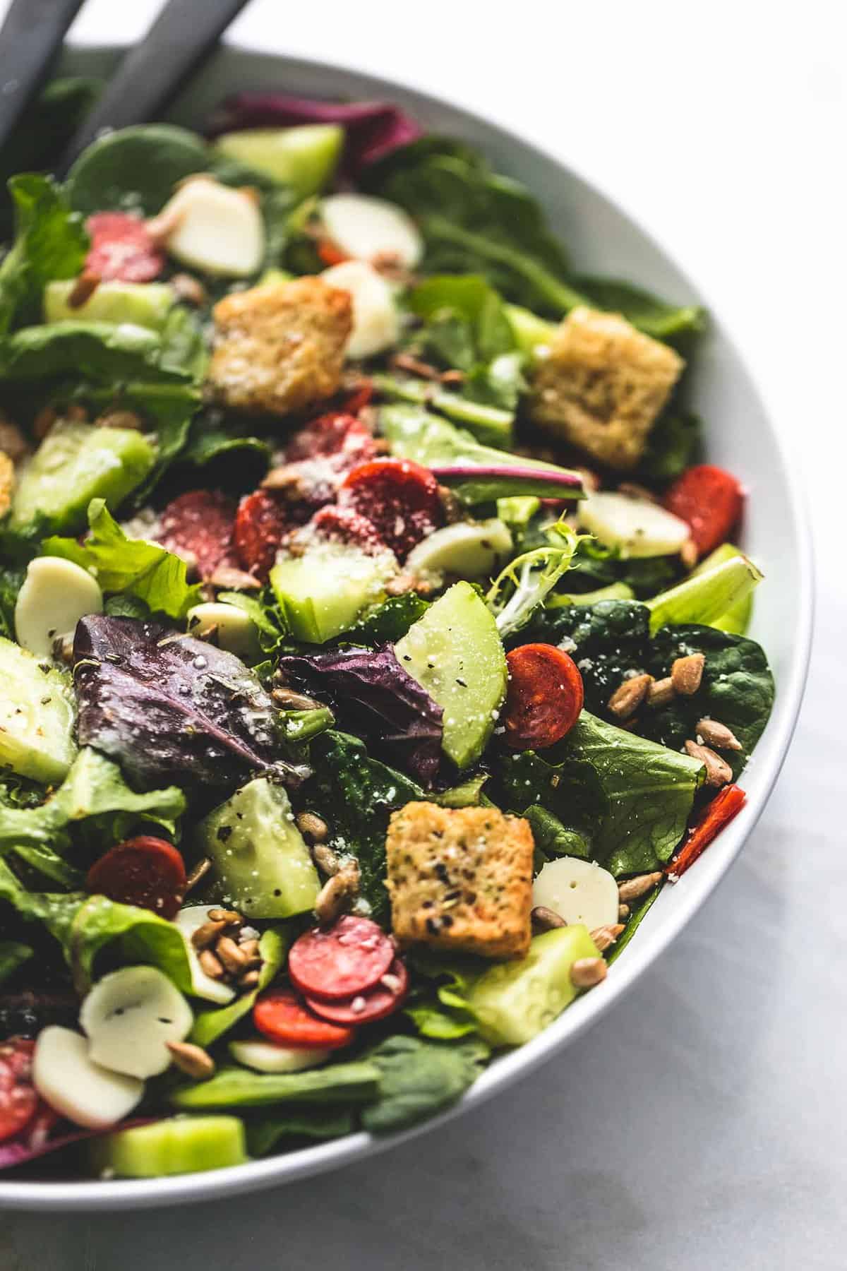 close up of Italian green salad with two serving spoons in a bowl.