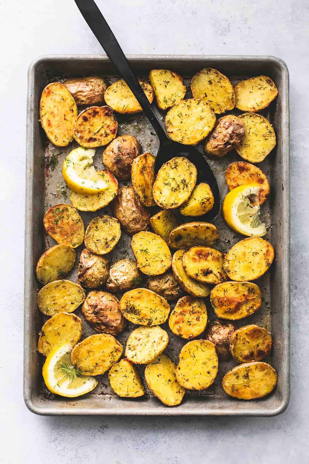 top view of oven roasted dill potatoes with lemon slices and a serving spoon on a baking sheet.