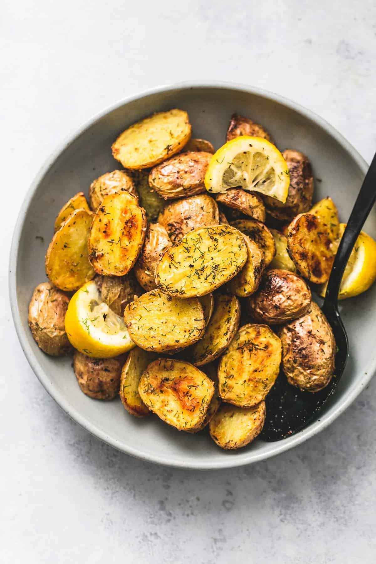 top view of oven roasted dill potatoes, lemon slices, and a spoon in a bowl.