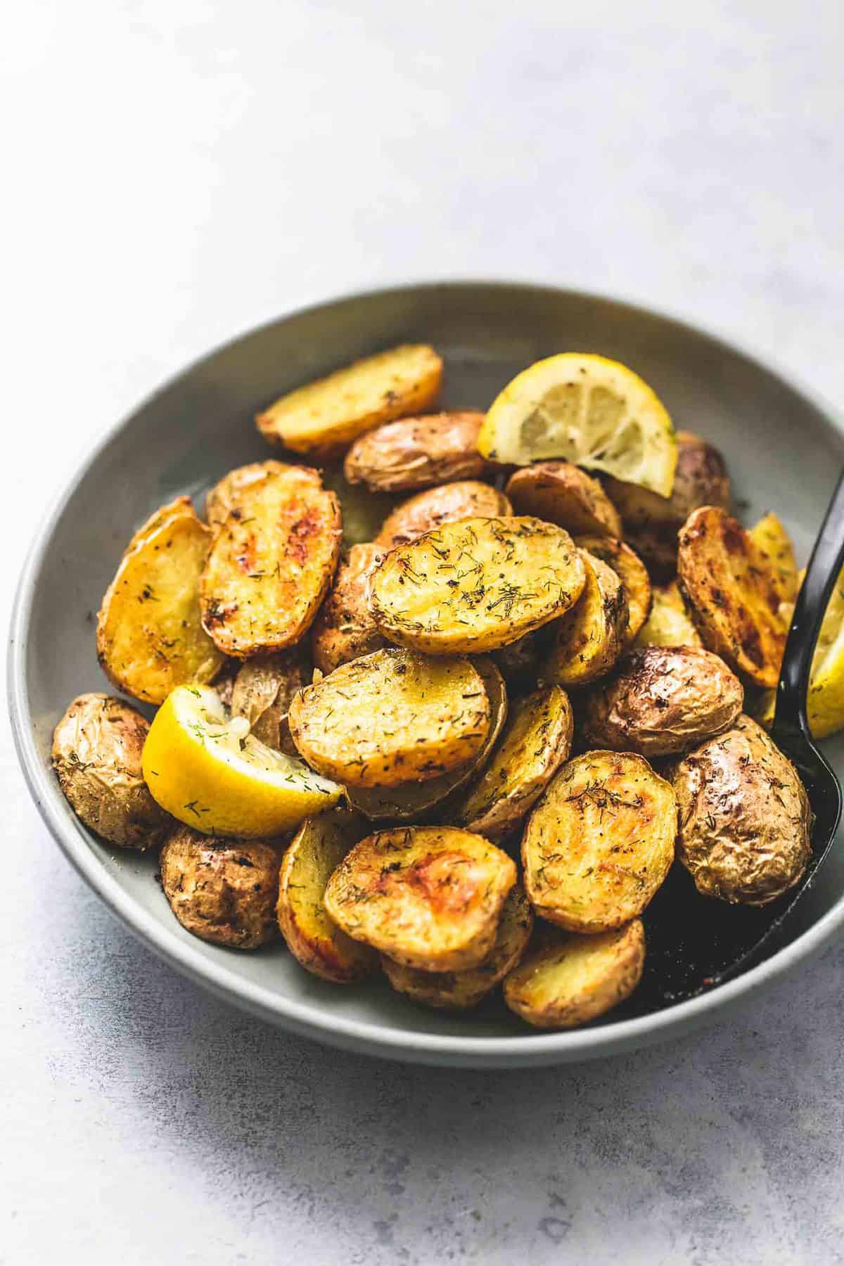 oven roasted dill potatoes with lemon slices and a fork in a bowl.