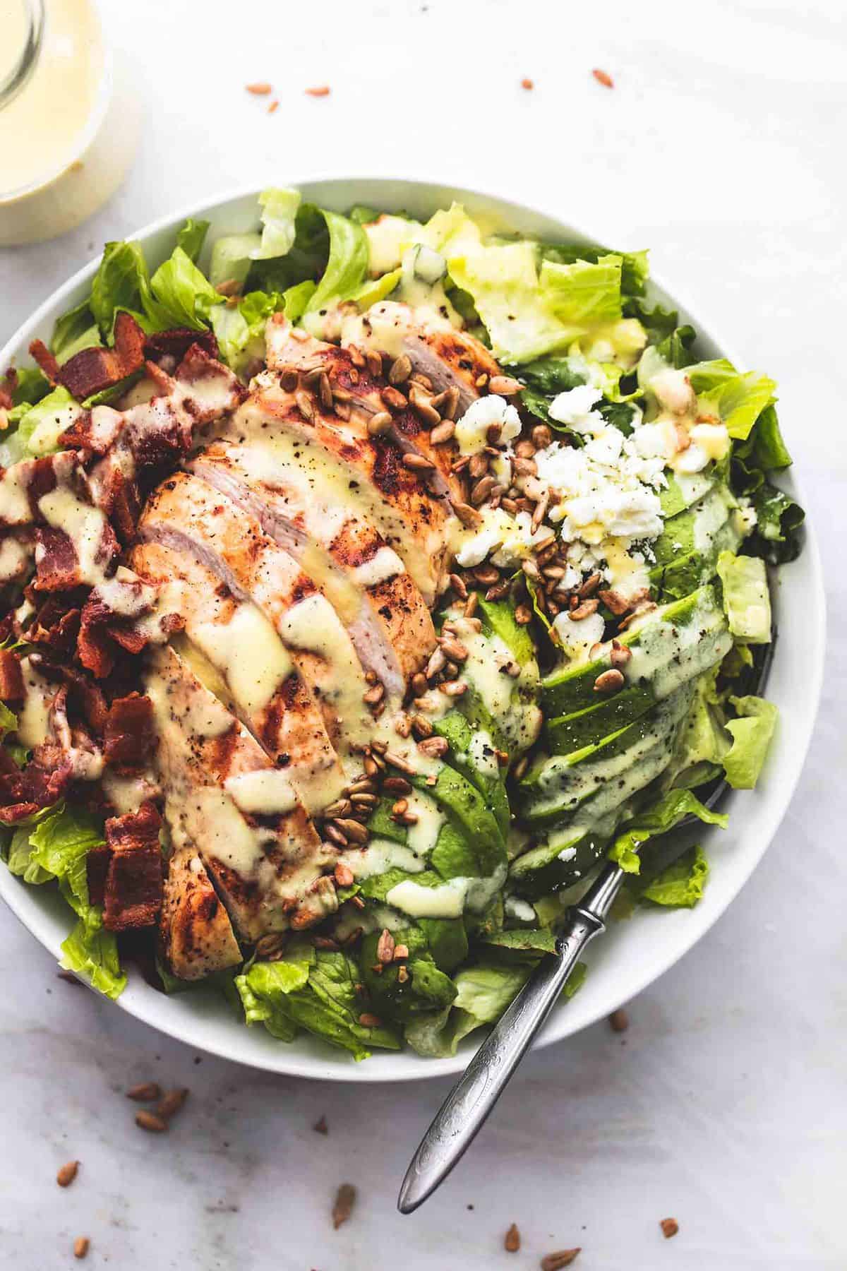top view of chicken, bacon and avocado salad with sweet vidalia onion dressing with a fork in a bowl with a jar of dressing barely visible on the side.