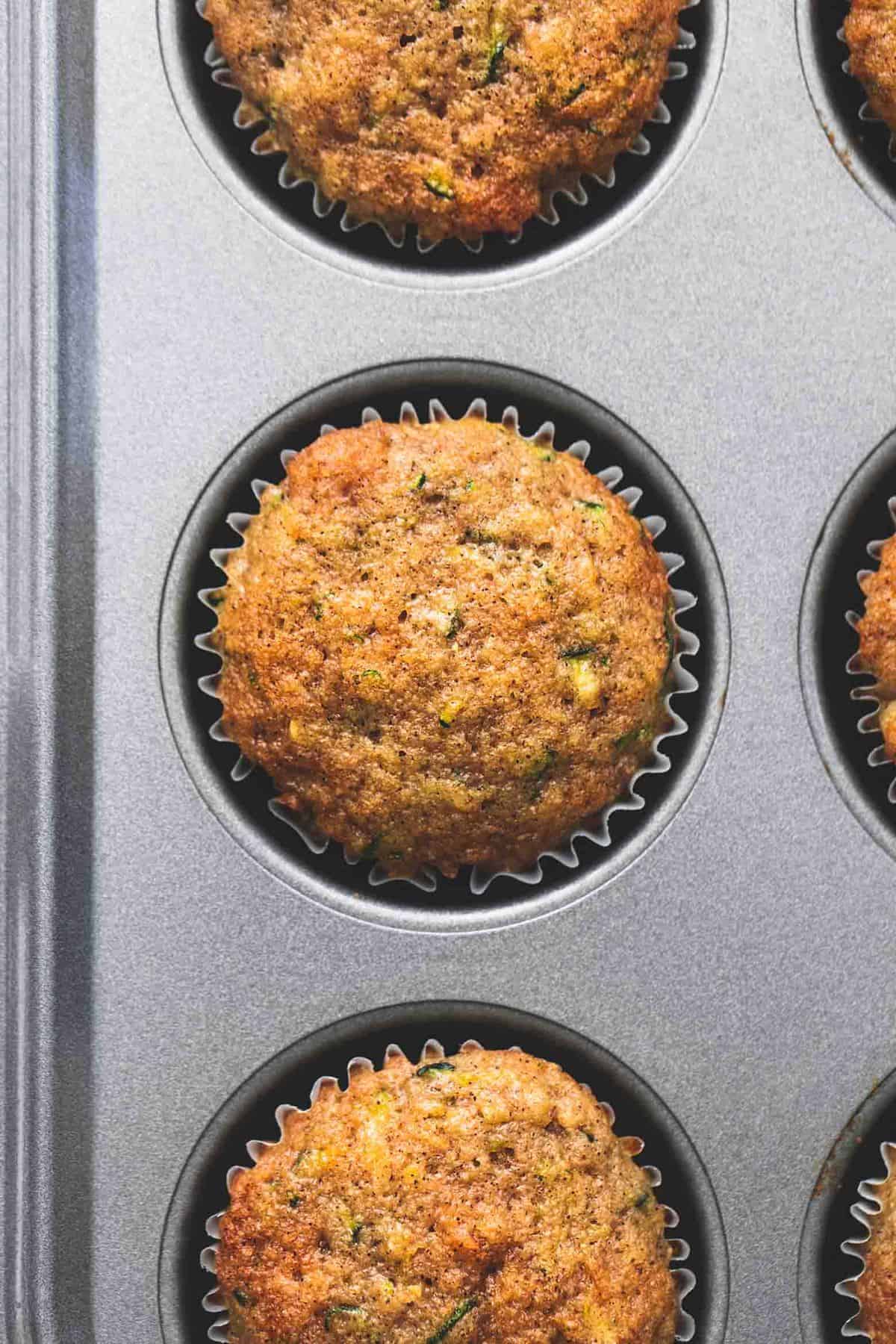 close up top view of a zucchini bread muffin with other muffins around it all in a muffin tin.