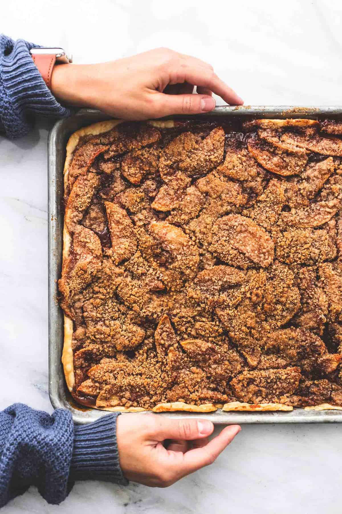 top view of a pair of hands holding a baking sheet of apple slab pie.