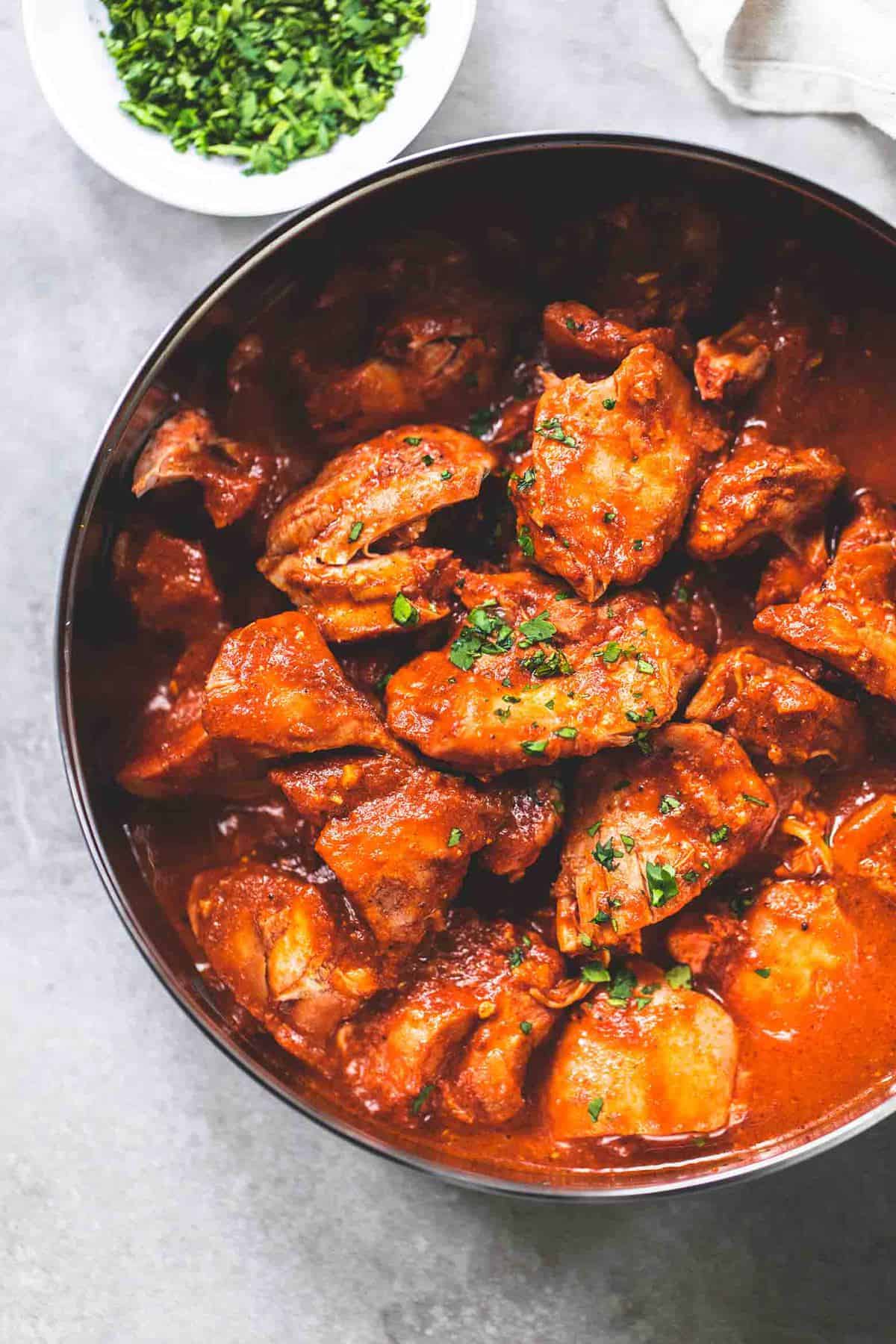 top view of instant pot chicken tikka masala in a pan with a bowl of cilantro on the side.