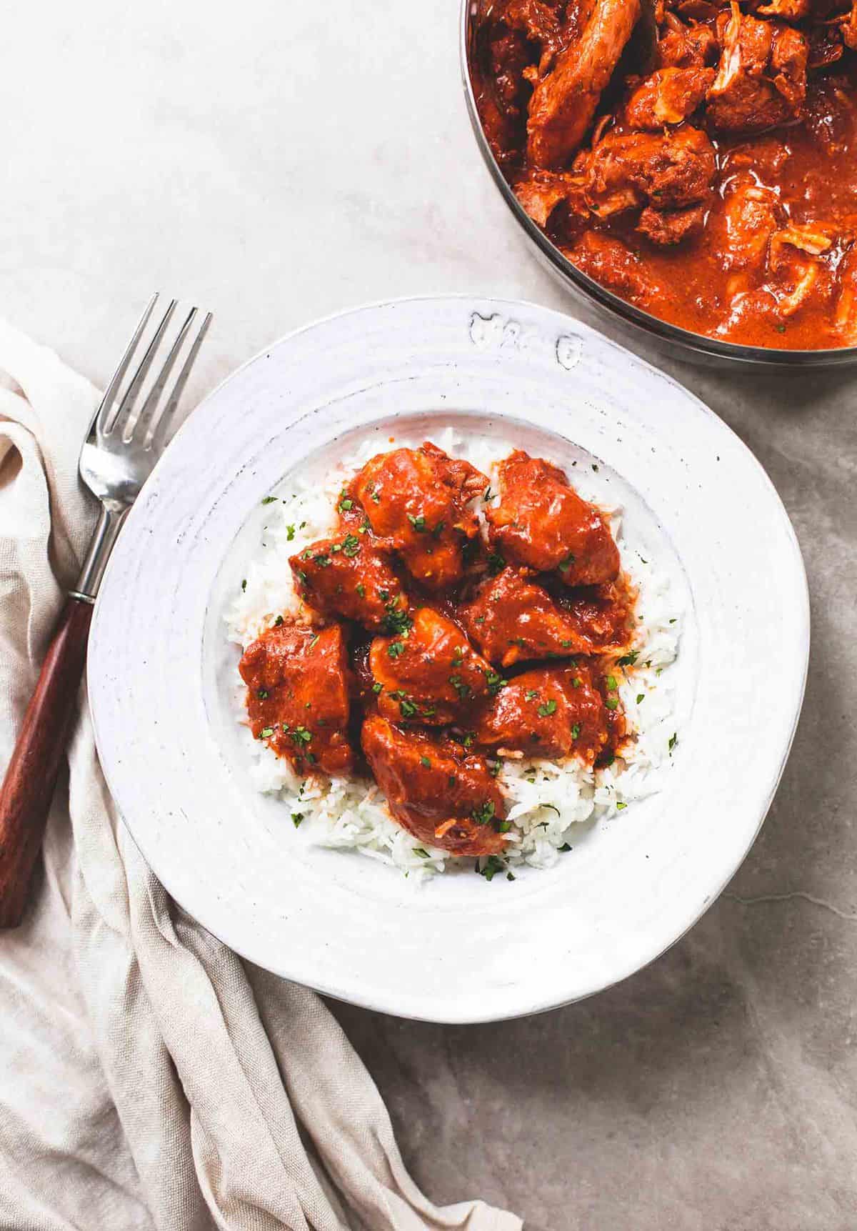 top view of instant pot chicken tikka masala on rice in a bowl with a fork and a pan of more chicken on the side.