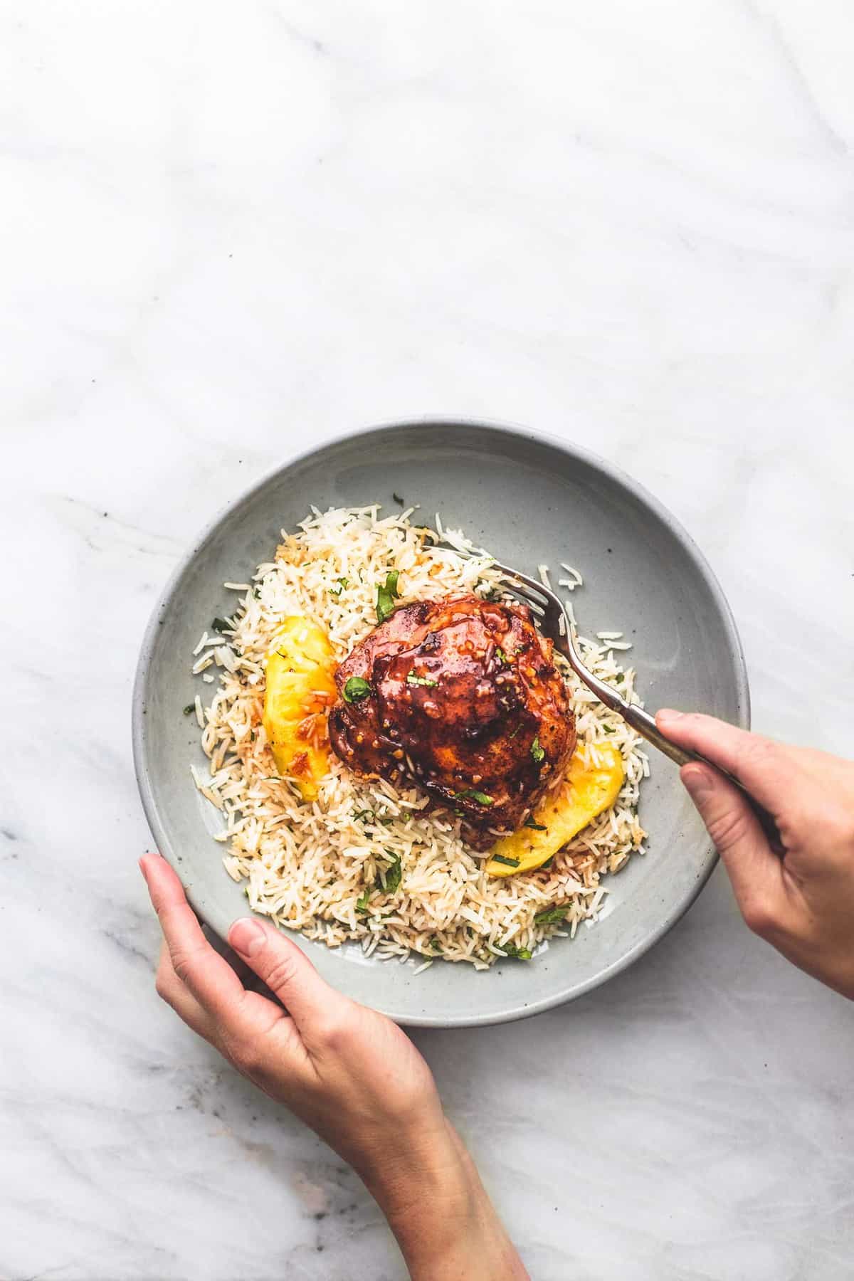 top view of Island glazed chicken and coconut rice on a plate with a hand holding one side of the plate and another grabbing a bite with a fork.